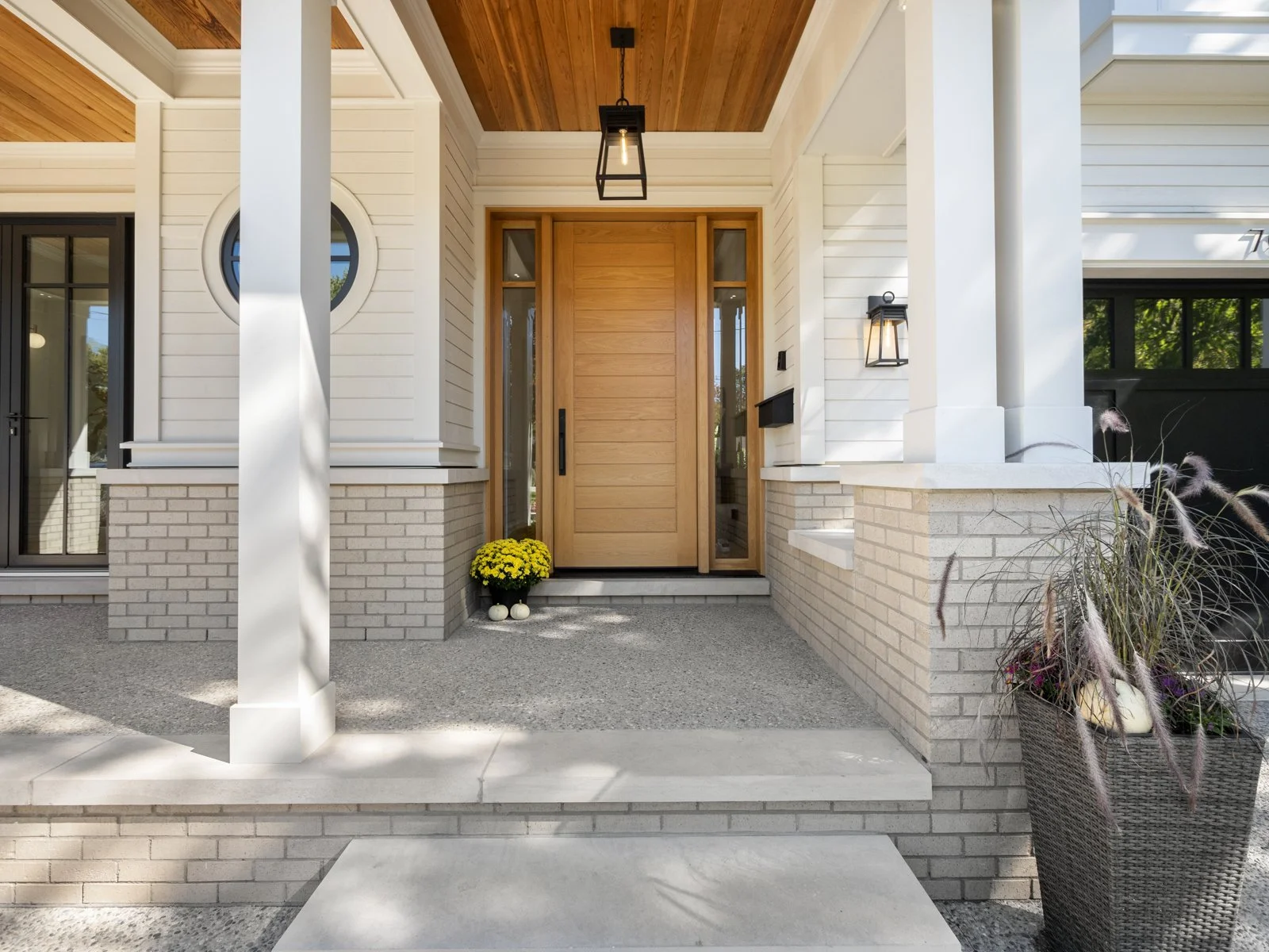 Front porch of a house with a wooden entry door, potted yellow flowers, and outdoor lighting fixtures
