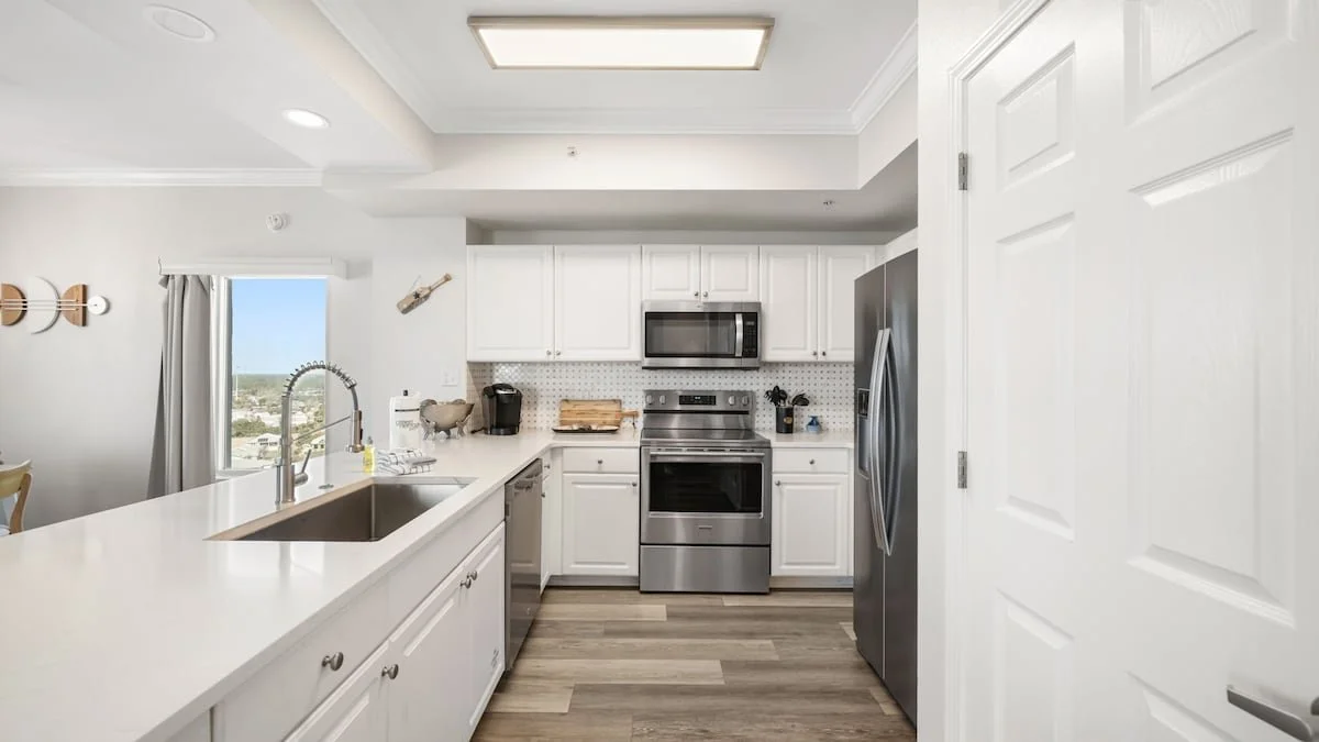 Modern kitchen with white cabinets, stainless steel appliances, a microwave, oven, refrigerator, and a window with a view of the city.
