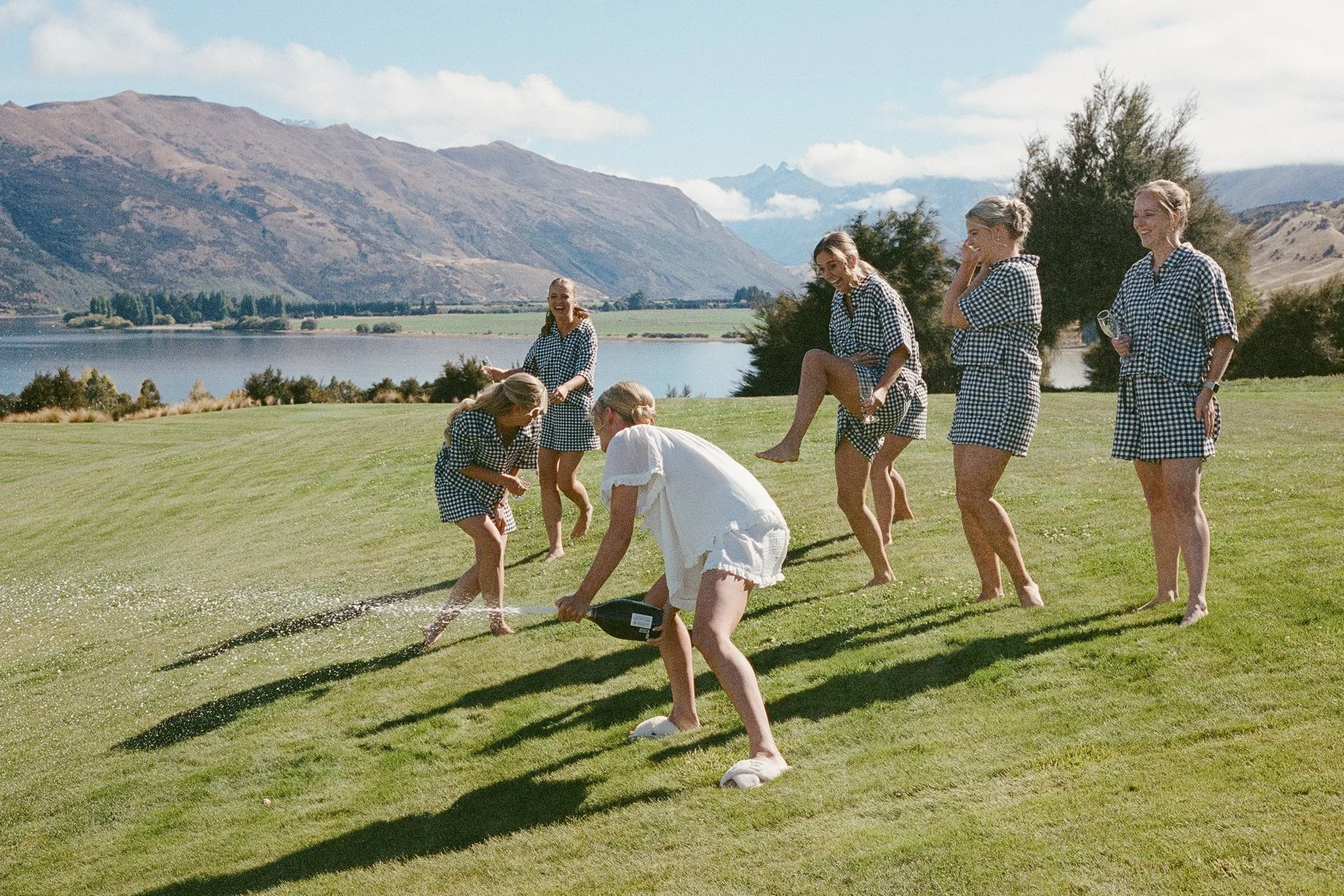 a 35mm film colour photo of a bride spraying her bridesmaids with champagne on the sunny morning of her wanaka wedding at dublin bay