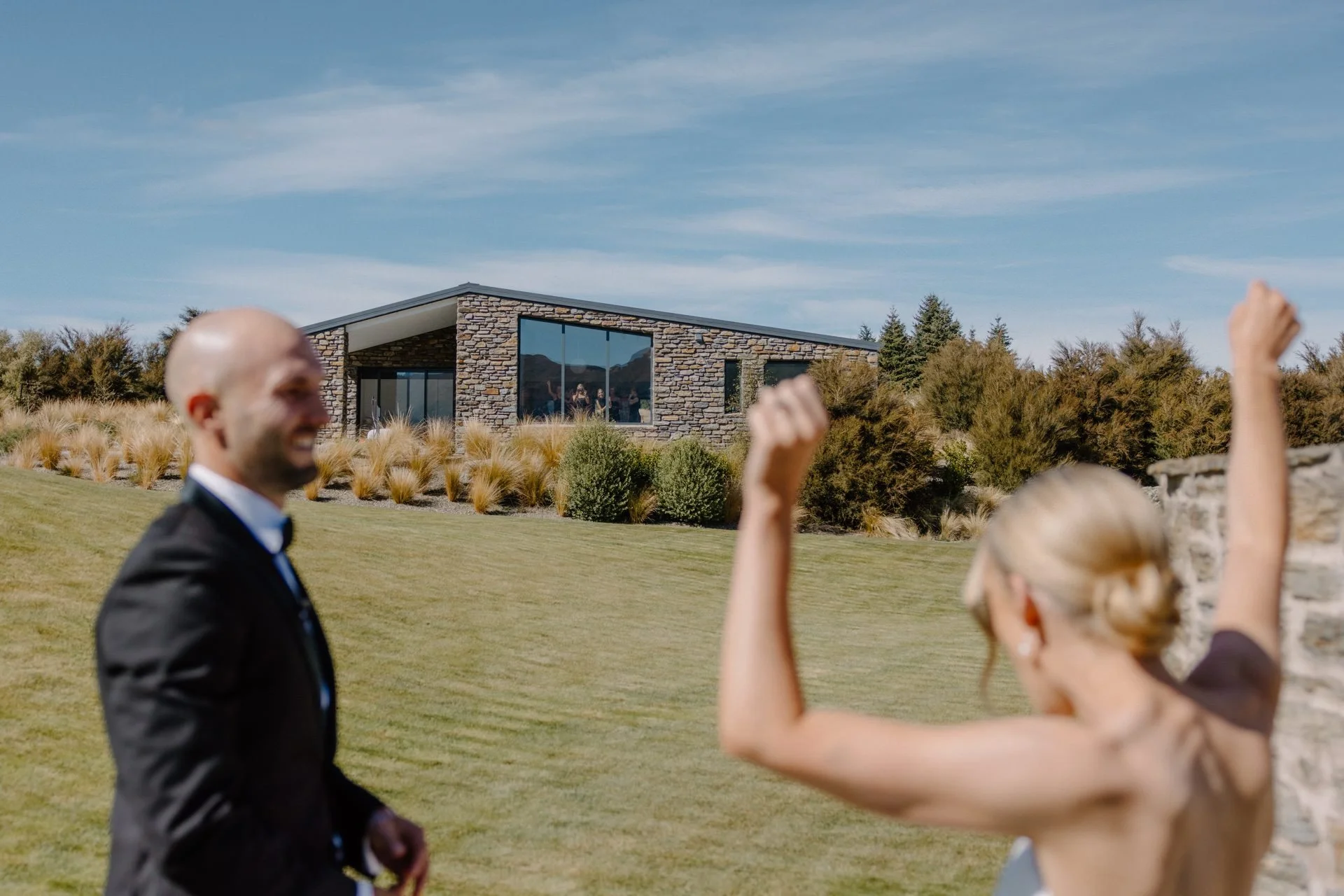 A bride and groom celebrate seeing each other for the first time on their wedding morning at dublin bay weddings. Their bridesmaids are cheering them on from the air bnb behind.