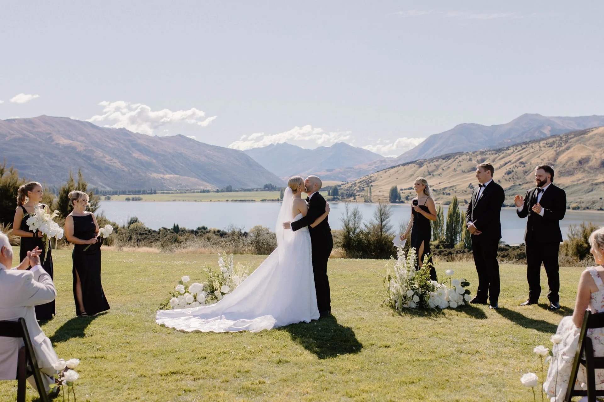 A bride and groom seal their wedding with a kiss standing in front of lake wanaka with mountains surrounding them at the beautiful dublin bay