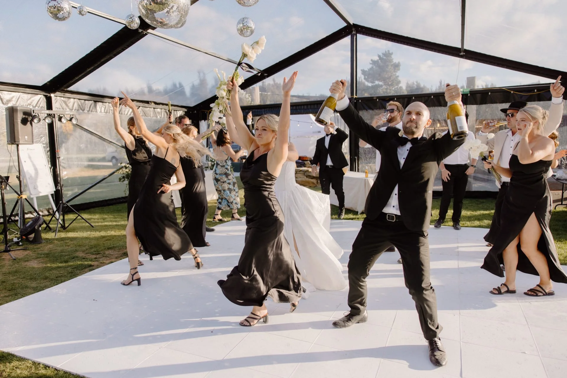 A bridal party led by the groom dance and spray champagne as they enter the clear marquee for their wedding reception at dublin bay in wanaka