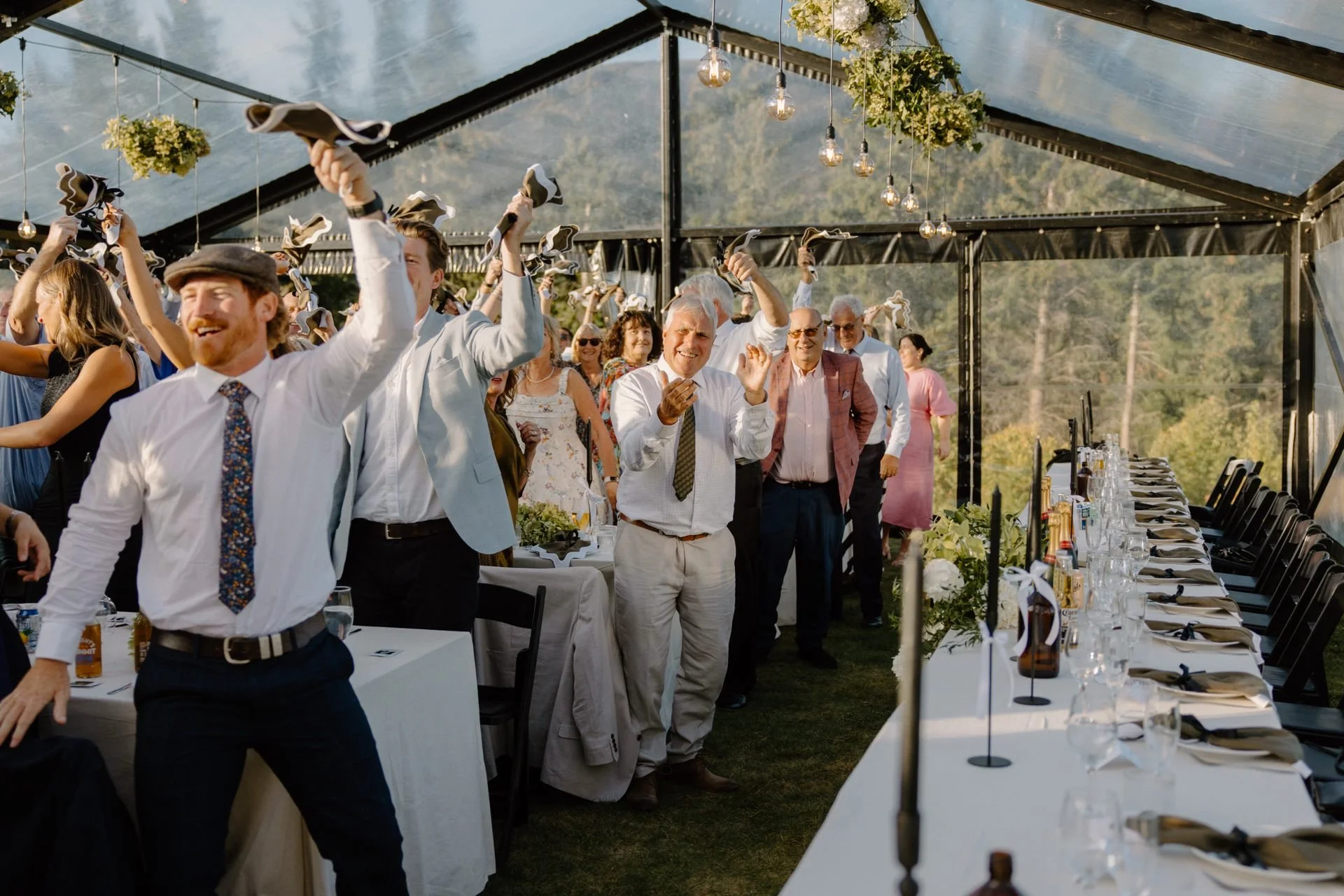 Guests wave their napkins above their heads as the bride and groom enter their clear marquee to start their wedding reception at dublin bay in wanaka.