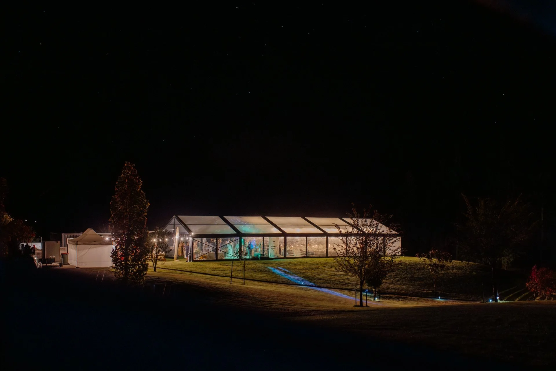 A clear marquee is lit up under the night sky at dublin bay in wanaka for a wedding celebration during summer.