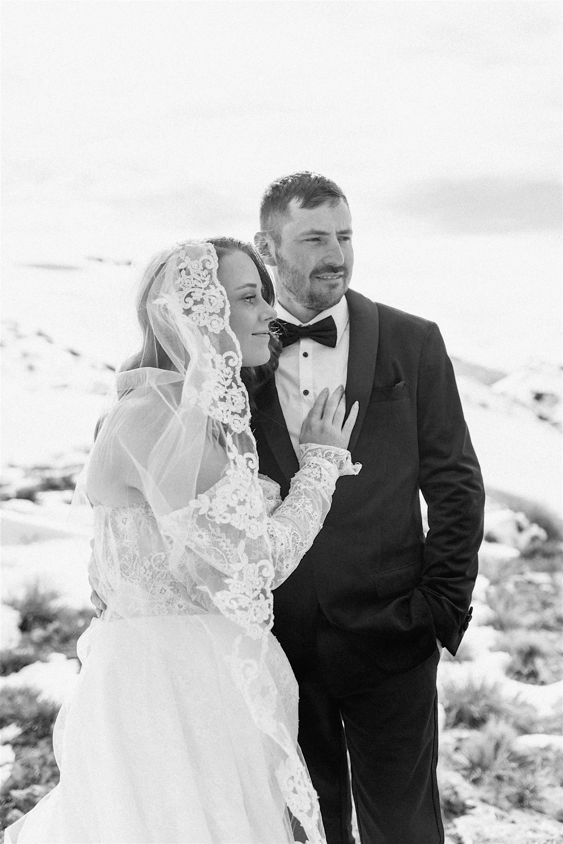  A black and white photo of a bride cuddling up to her groom on a snowy mountain in wanaka on their destination wedding elopement in spring. 