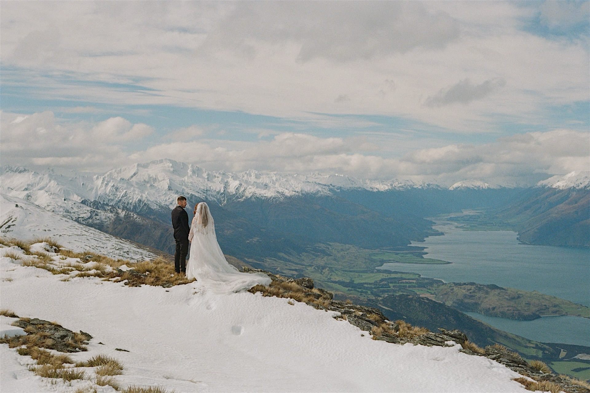  A bride and groom stand high on a snow covered mountain in Wanaka on their wedding day, taken on 35mm film 