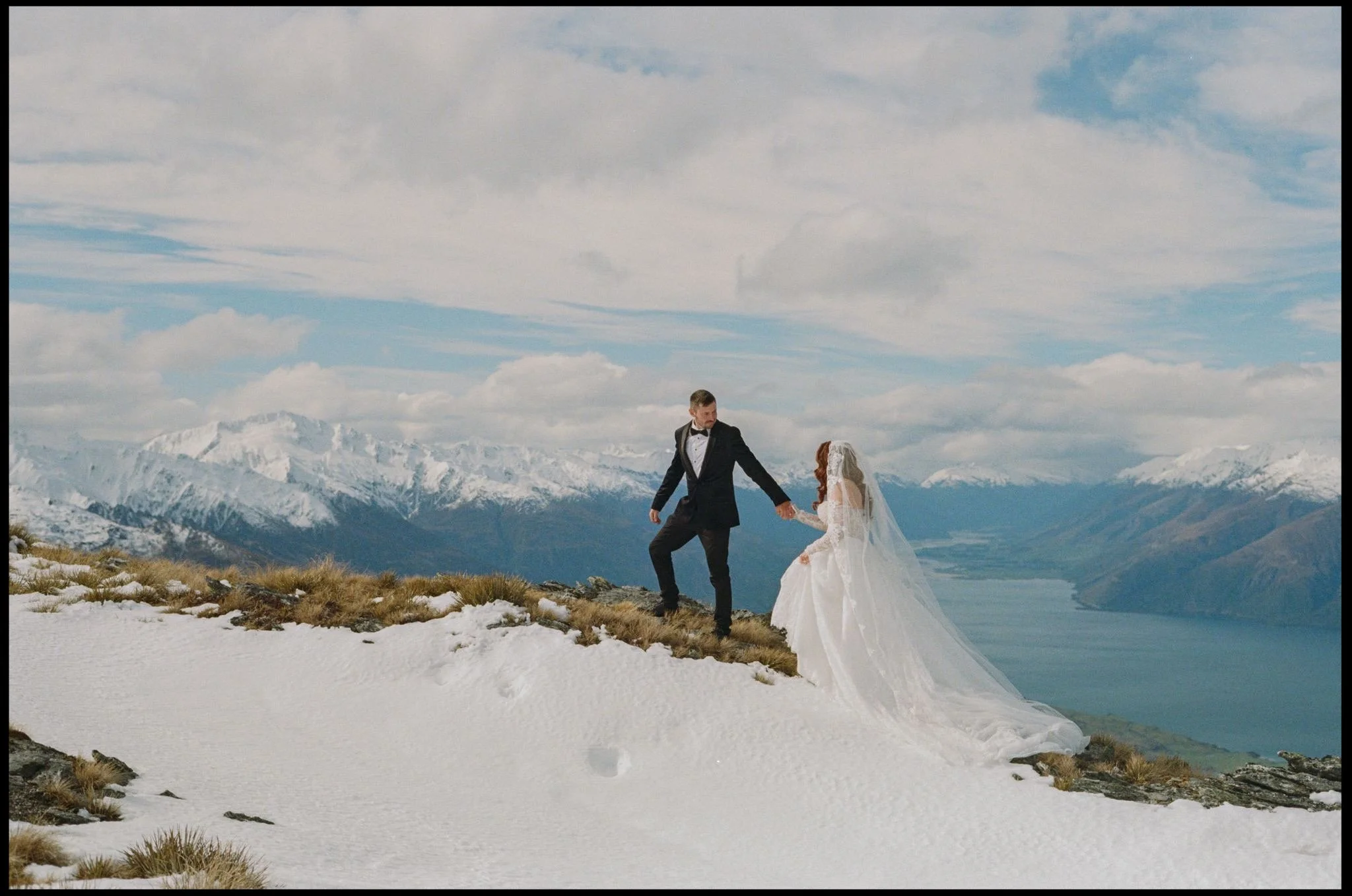 A married couple walk hand in hand on a snowy mountain top on their wanaka elopement