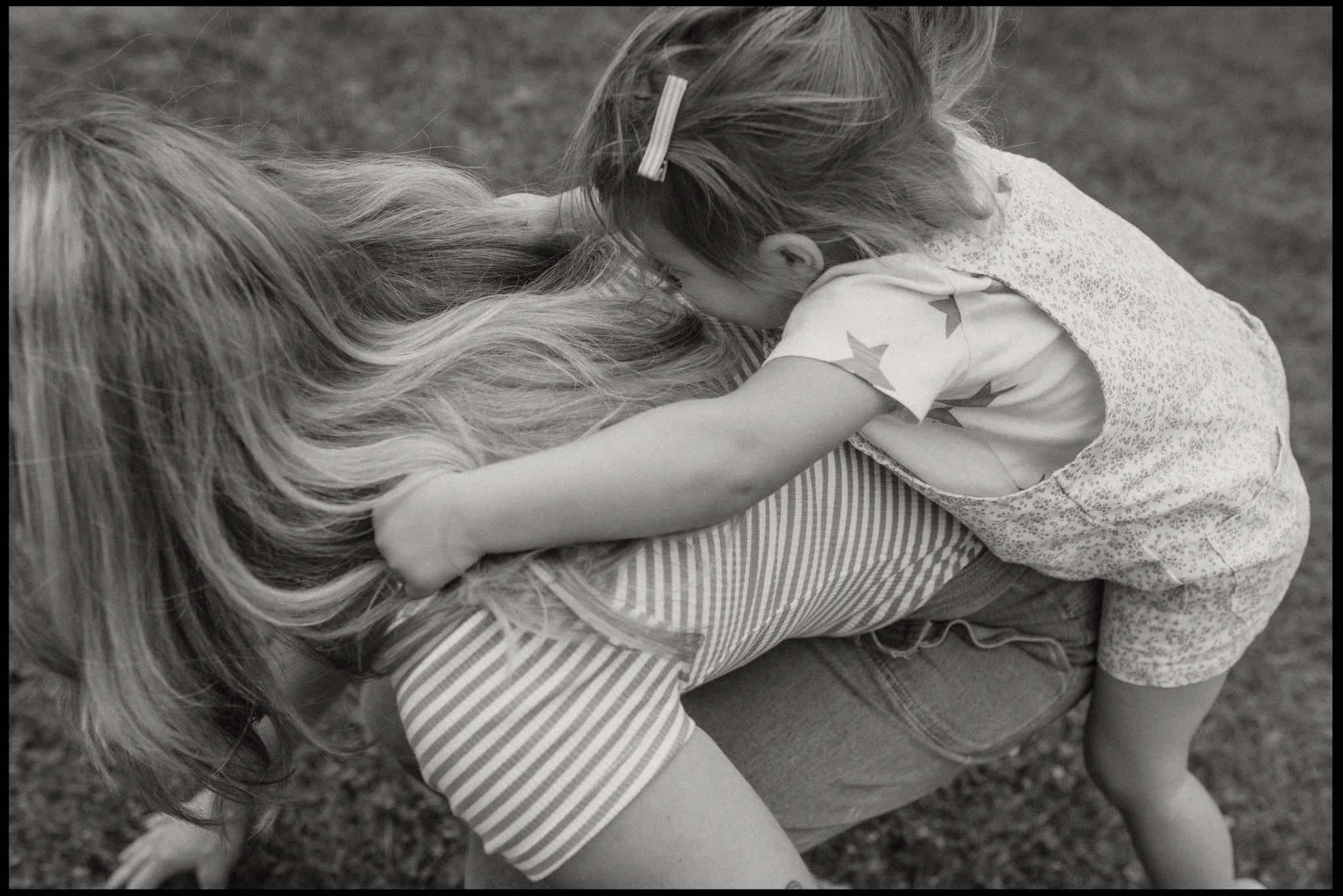A black and white photo of a little girl climbing on her mums back