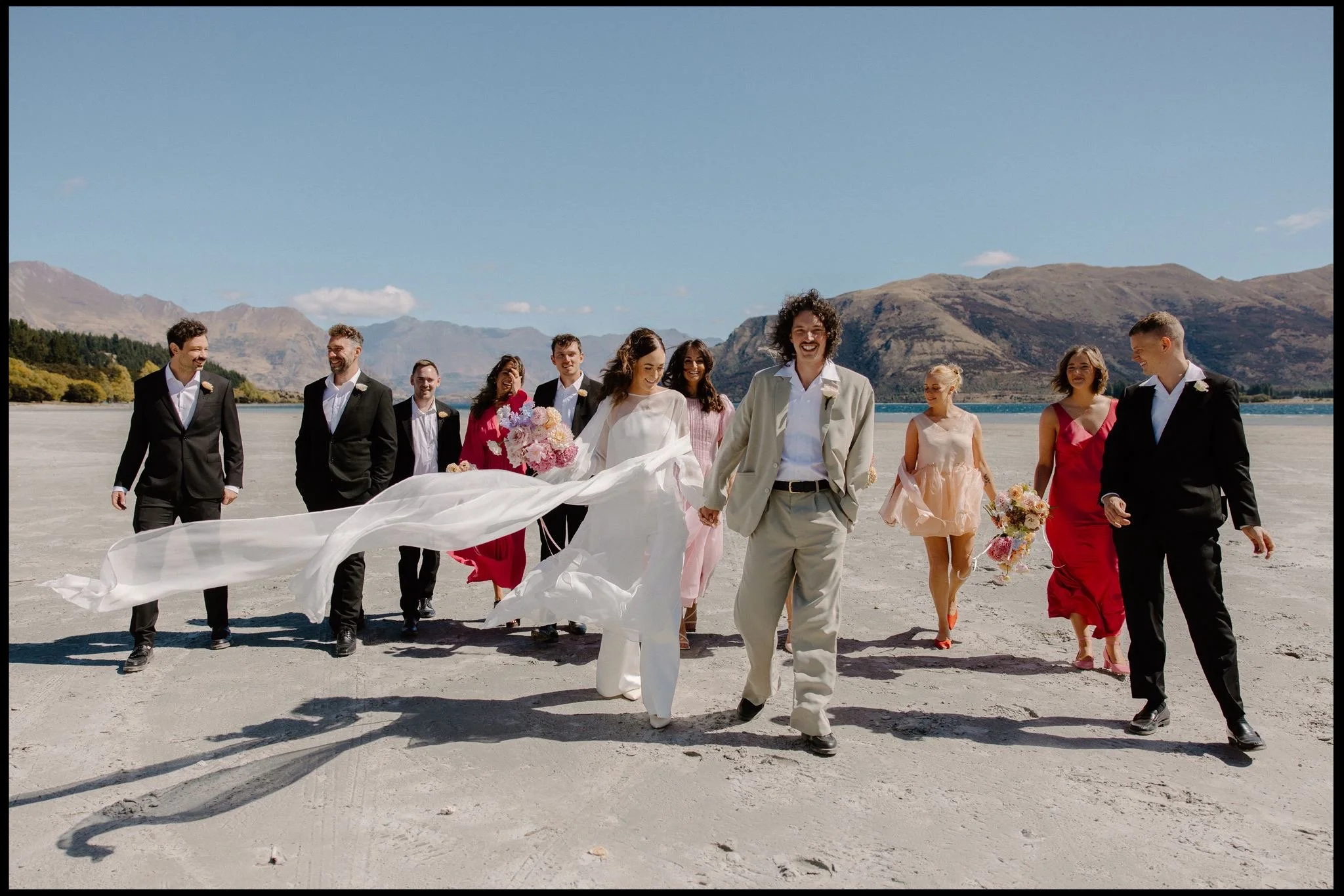 A bridal party walk along the lake on their wanaka wedding party on a summers day