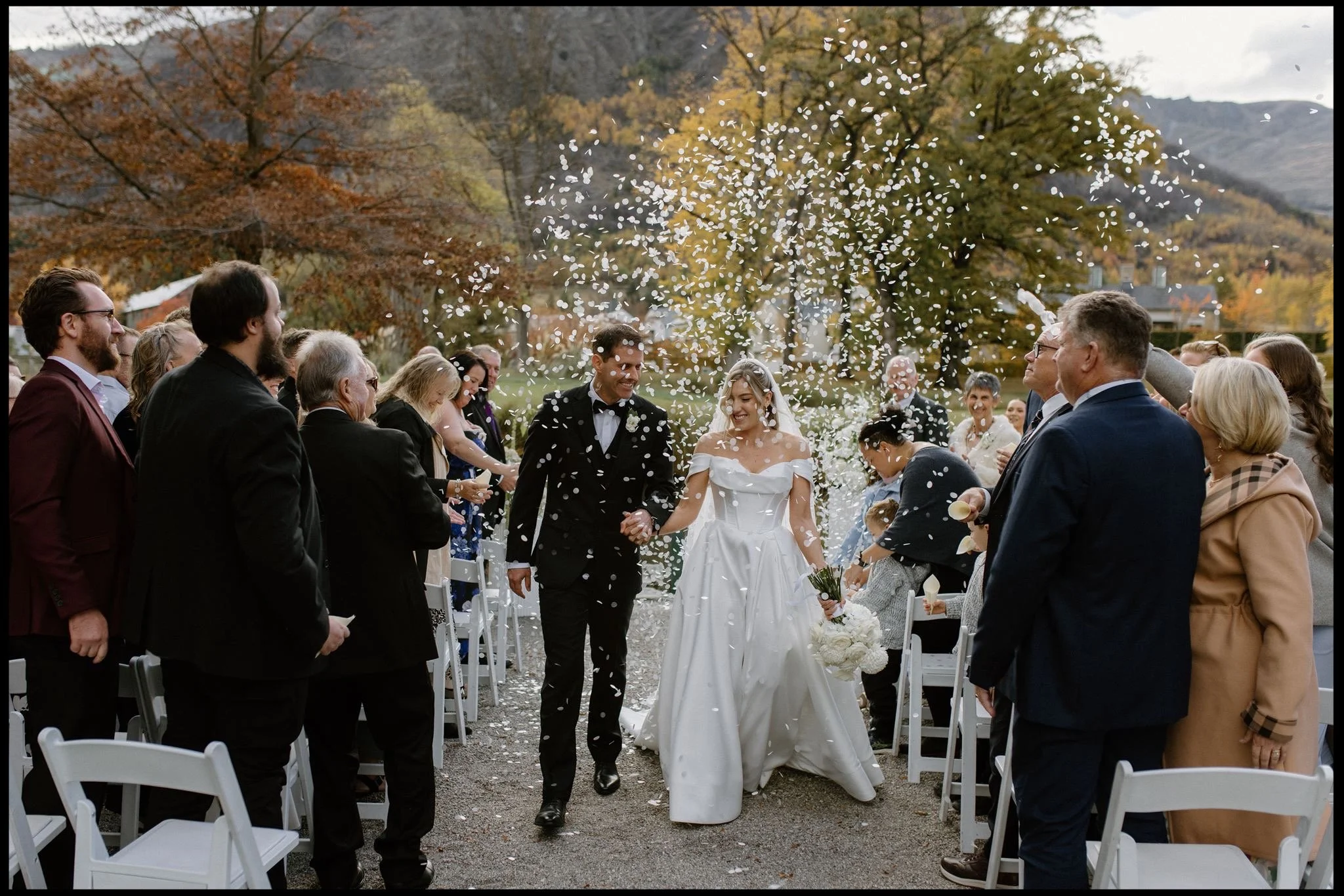 A bride and groom walk down the aisle in a shower of confetti on their wedding day at Millbrook resort in Queenstown in autumn