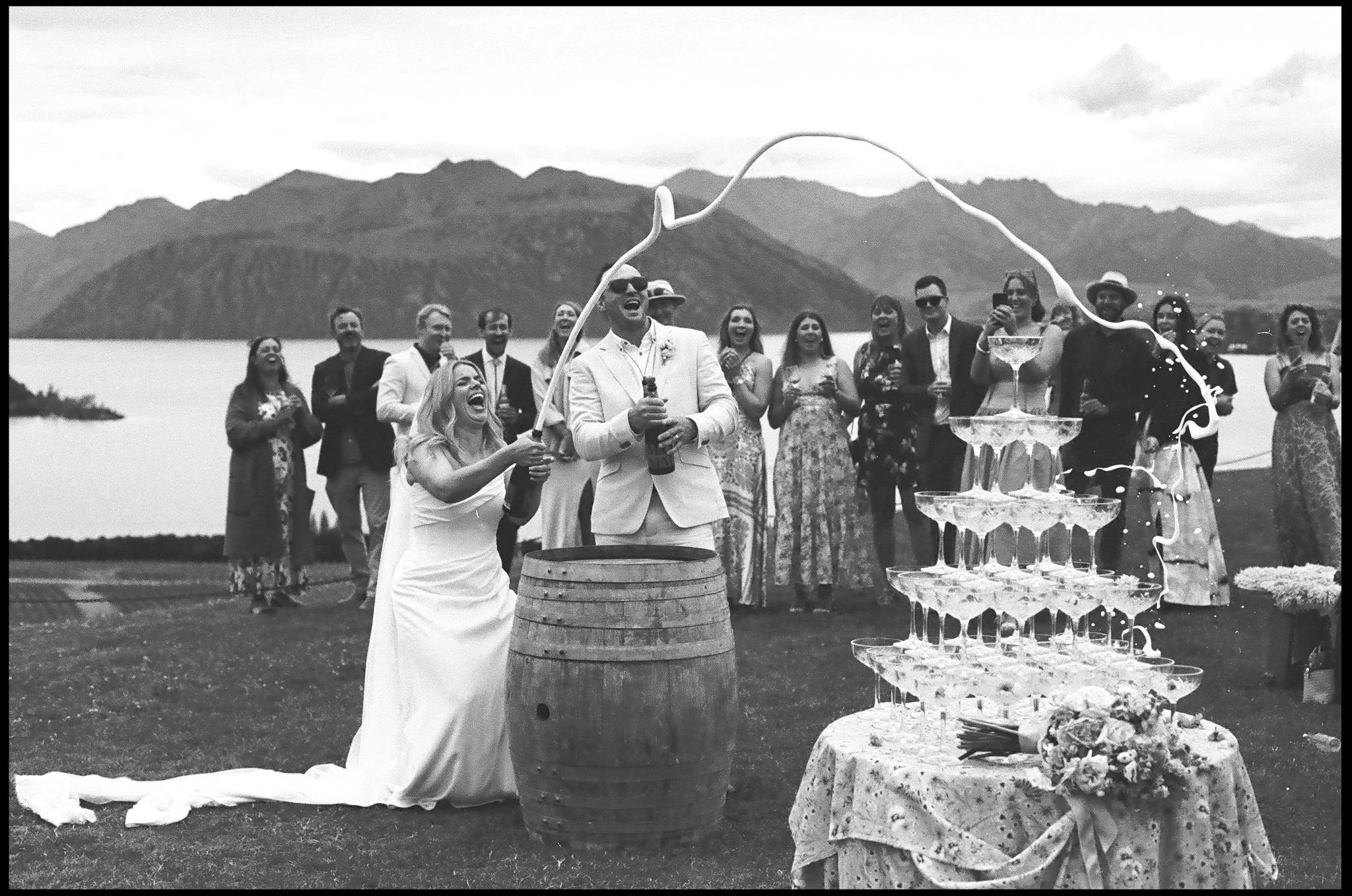 A Bride and Groom spray champagne over a tower on their wedding day at Rippon Vineyard in Wanaka