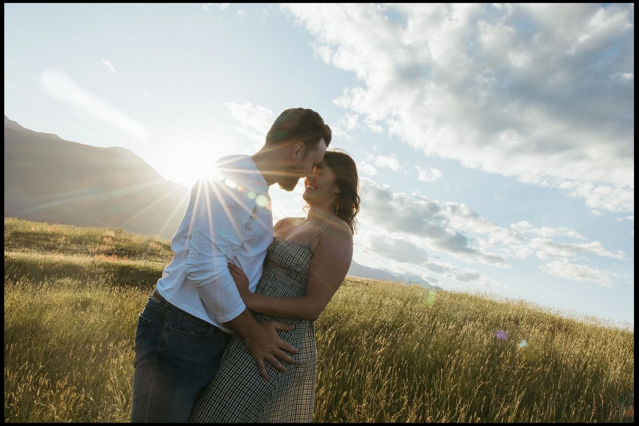 A couple cuddle against the backdrop of Mt Roy in Wanaka under the setting sun on their couples shoot