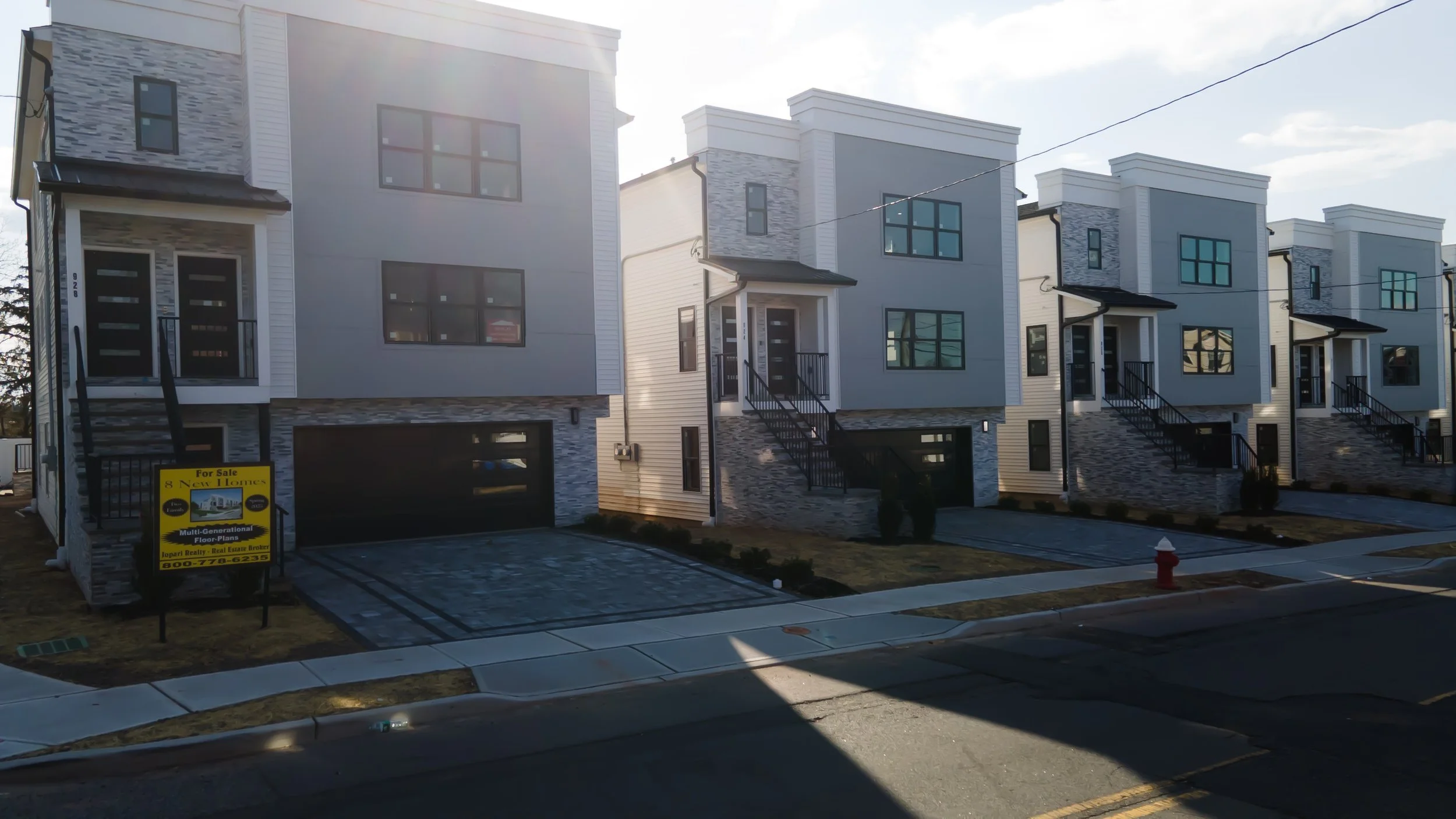 Row of newly constructed modern townhouses with stairs leading to front doors, some with stone accents, in a neighborhood under sunlight.
