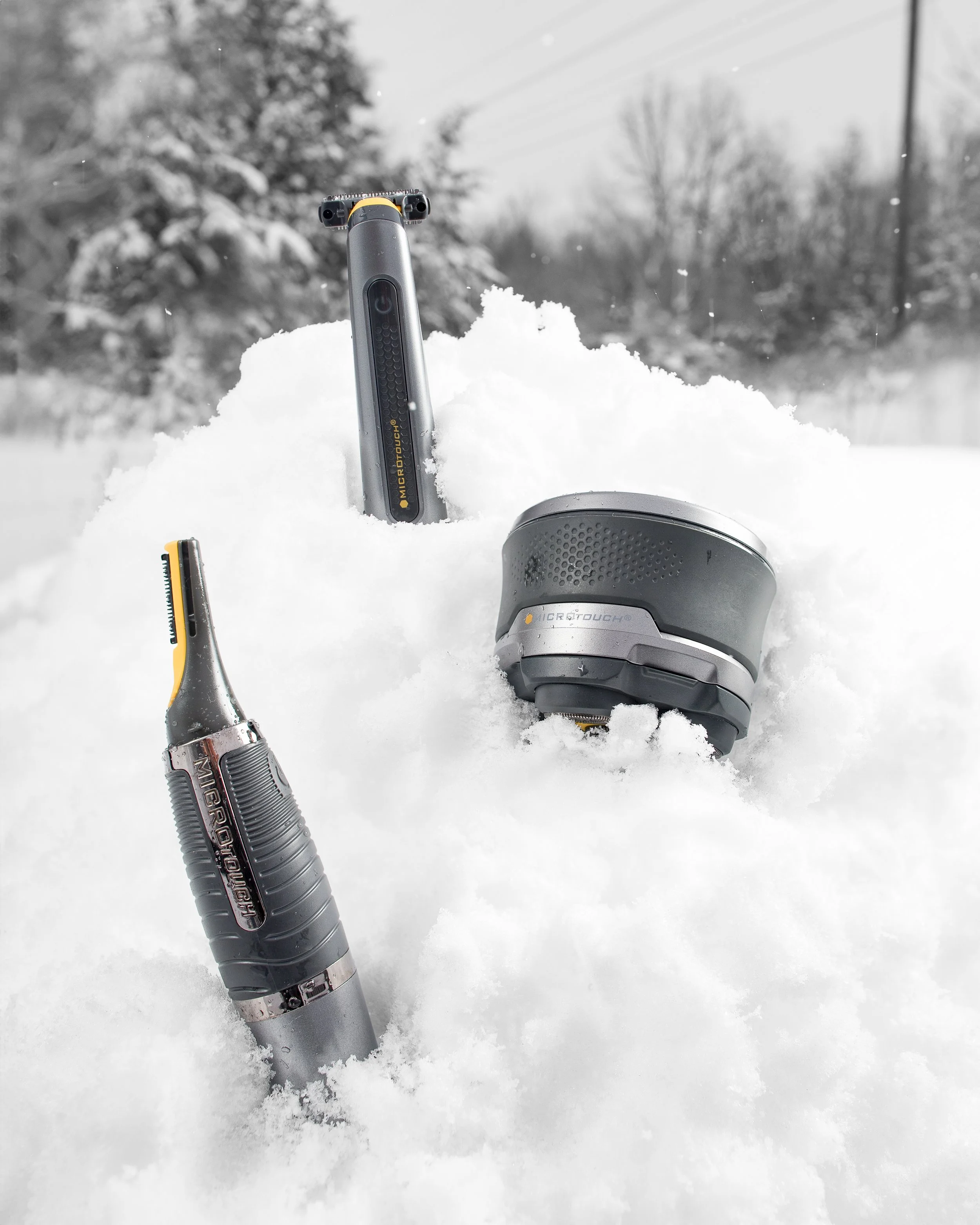 Three grooming tools partially buried in snow outdoors, with trees and power lines in the background.