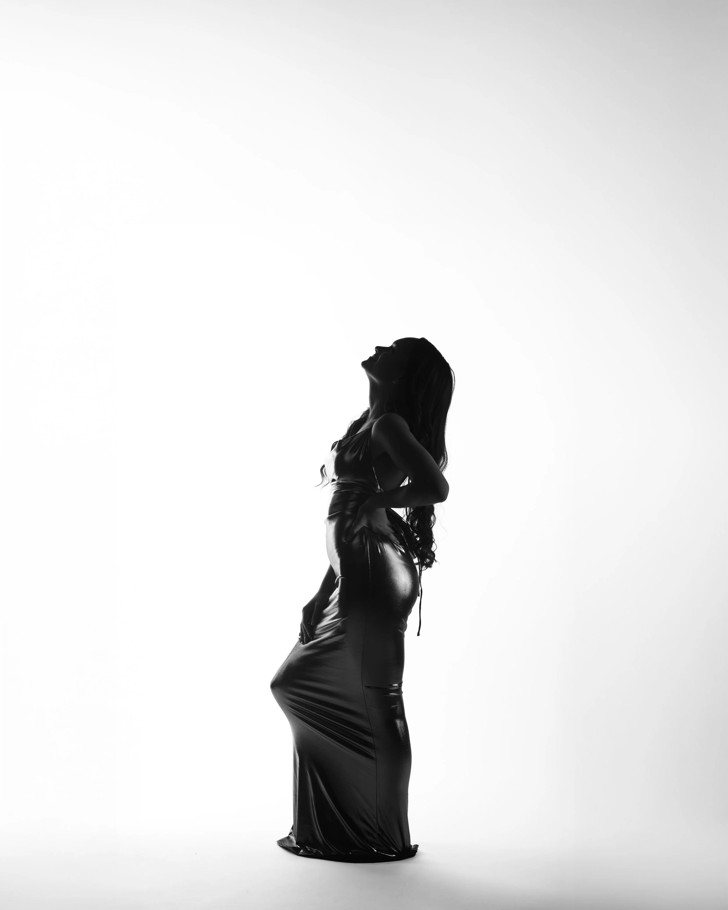 Silhouette of a woman in a shiny dress, standing with her head tilted back and hand on her hip, against a white background.