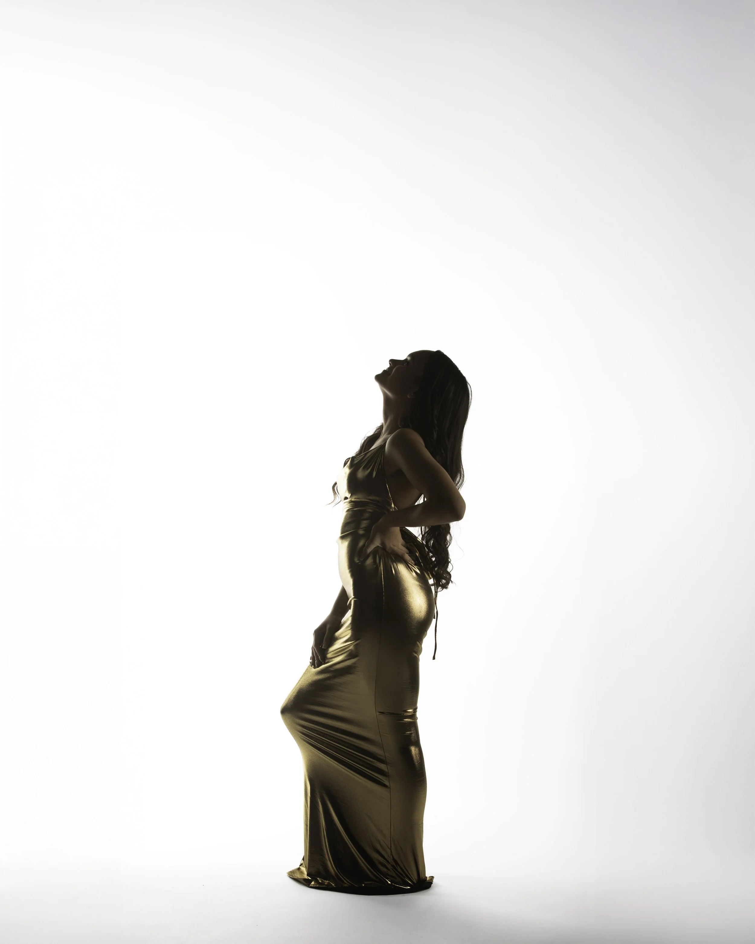A woman in a shiny gold dress posing with her head tilted back against a white background.