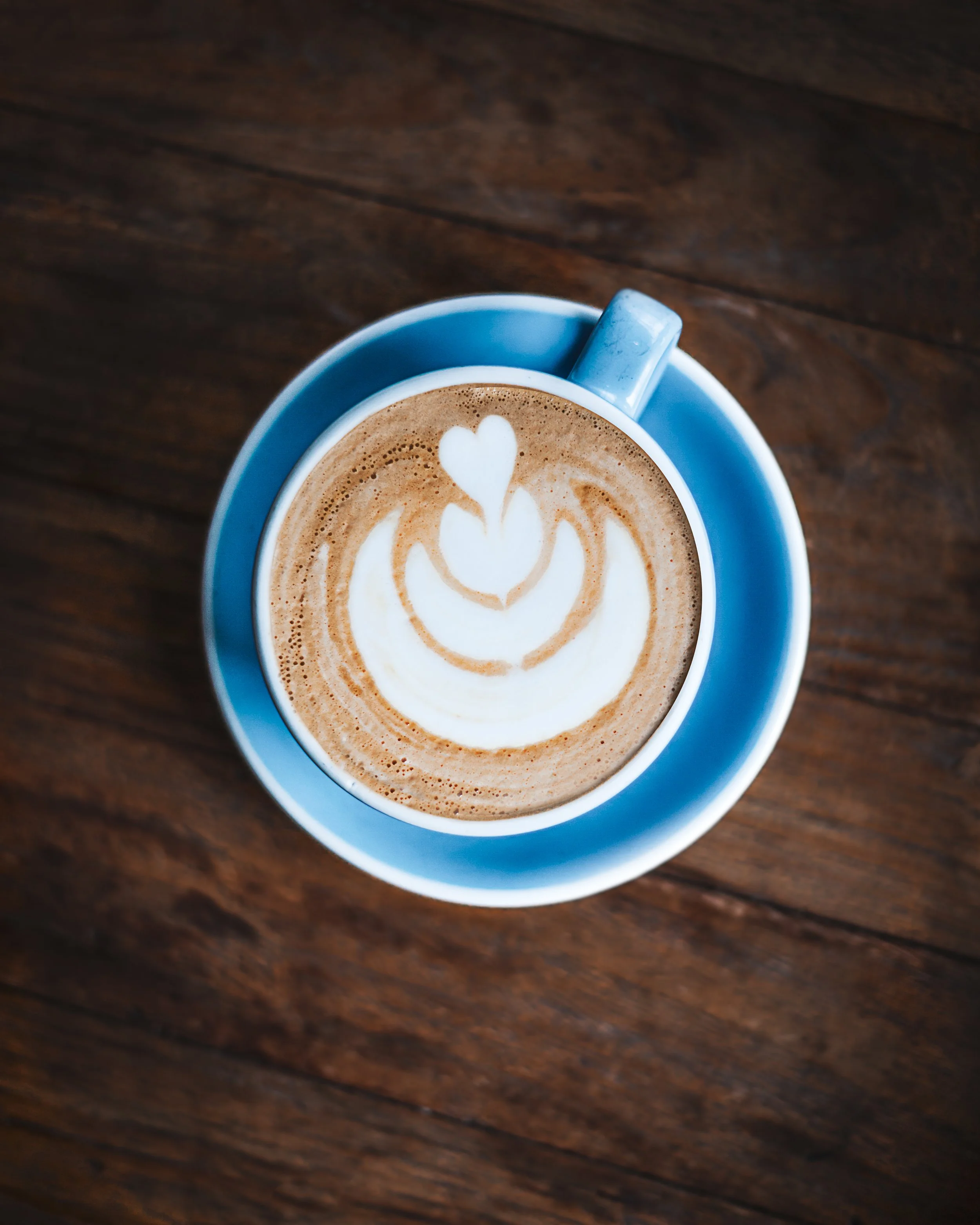 Blue cup of coffee with latte art in a heart shape placed on a wooden table.