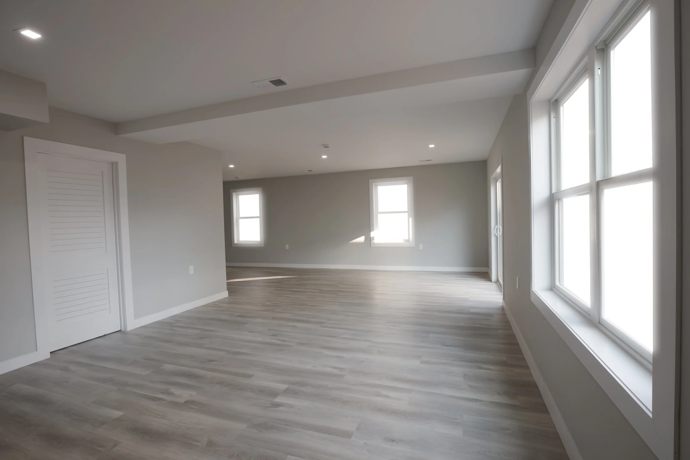 Empty living room with light gray walls, large windows, and light wood flooring.