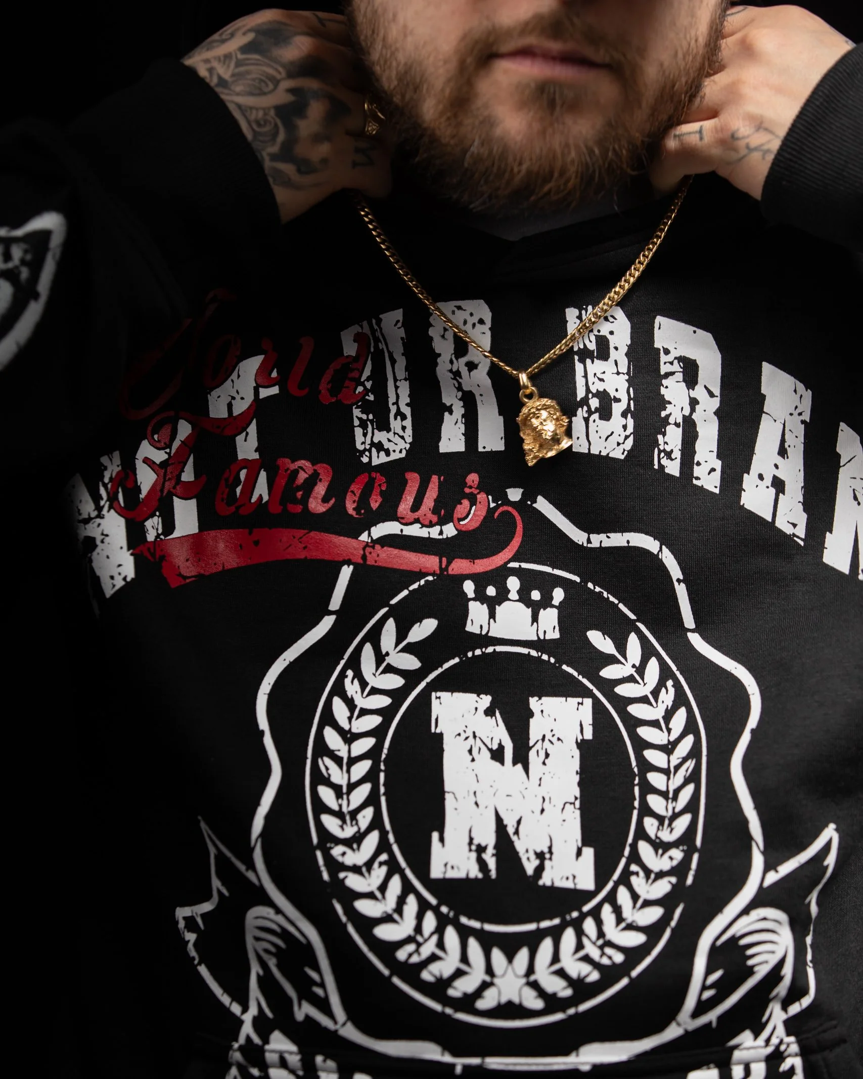 Close-up of a man wearing a black hoodie with white and red graphic design and a gold chain with a skull pendant.