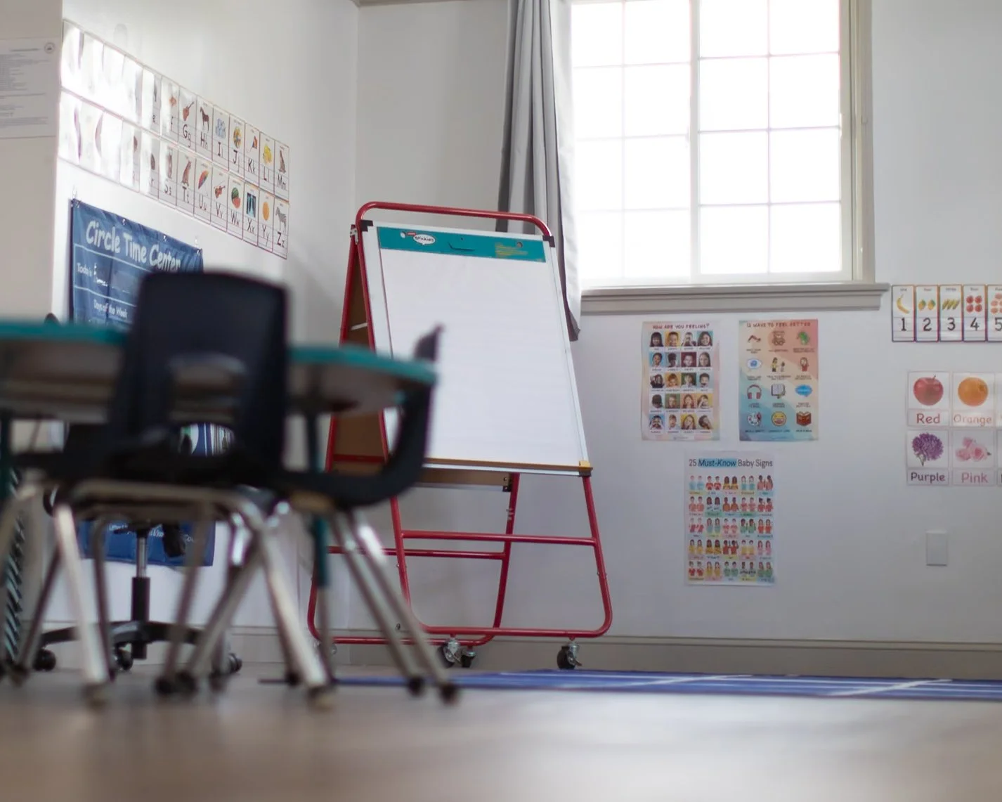 Empty classroom with small chairs, a whiteboard on wheels, and educational posters on the wall.