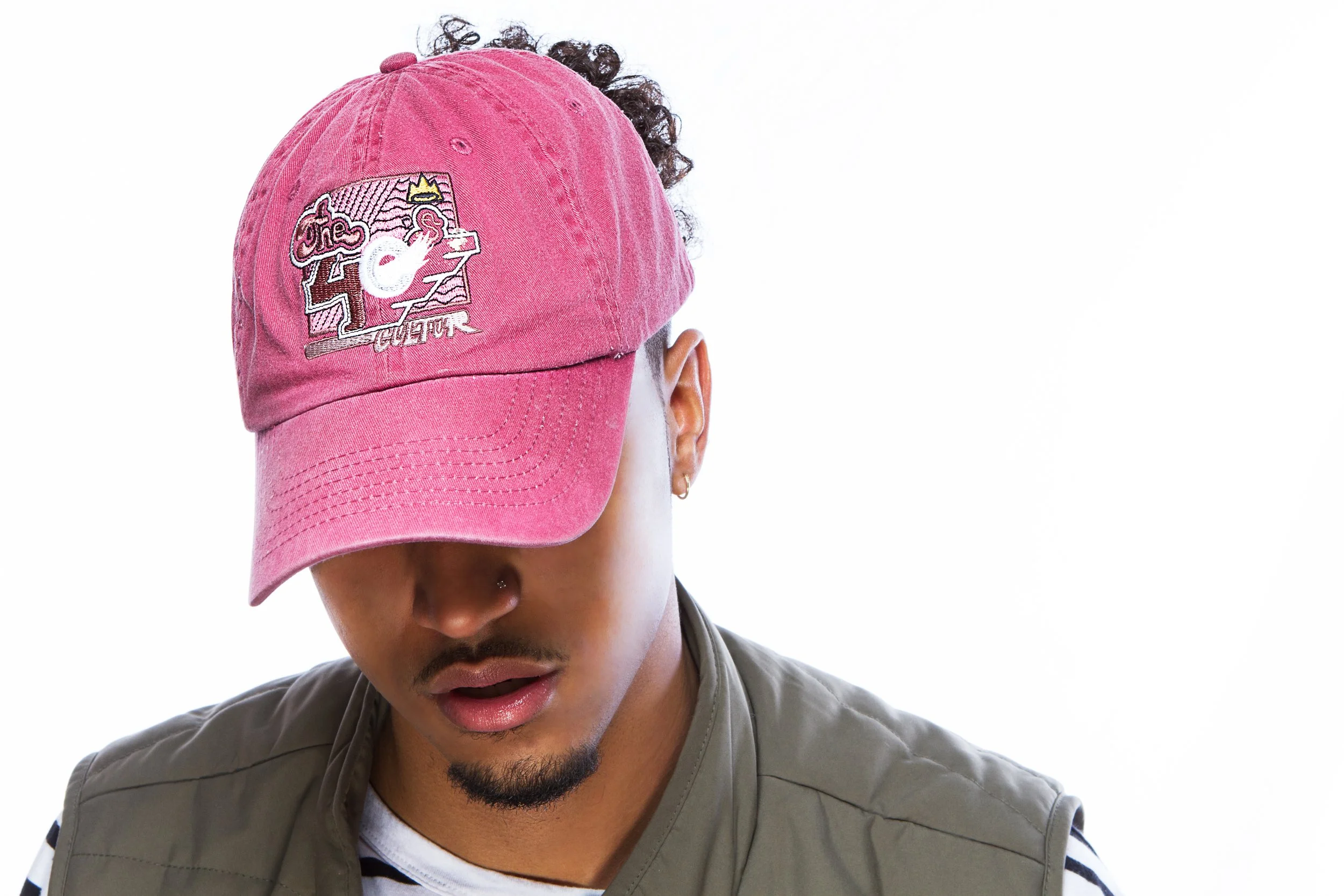 Person wearing a pink baseball cap with embroidered design, looking down, against a white background.