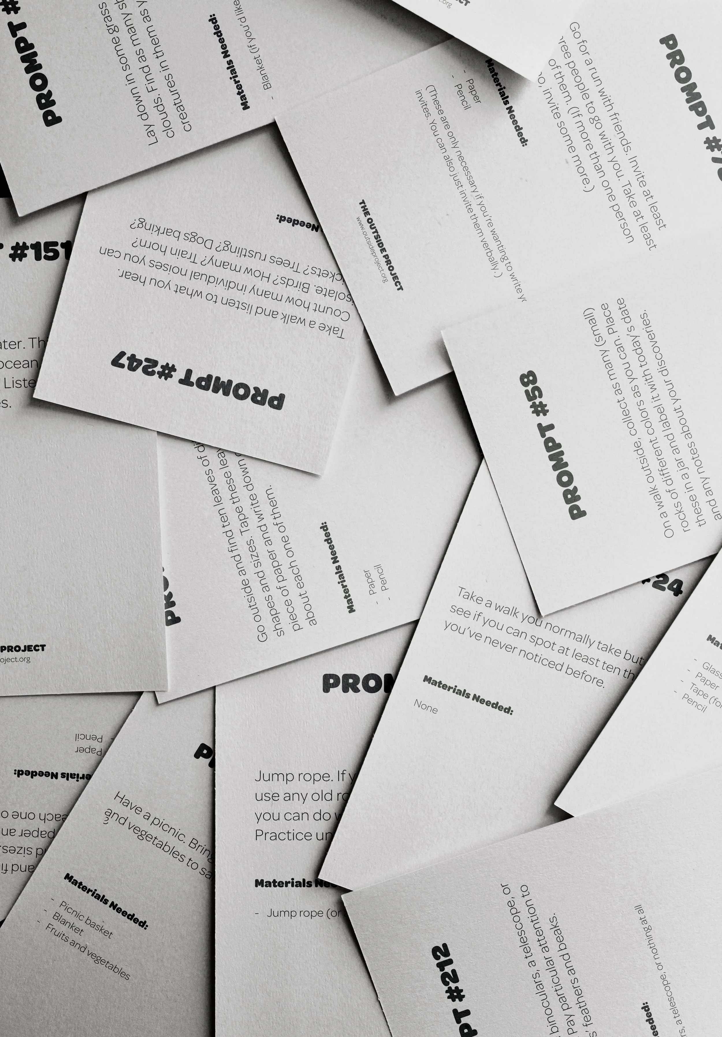 Collection of printed activity instruction cards with bold project numbers, scattered on a surface. The cards contain step-by-step instructions and list of materials needed for various outdoor activities.