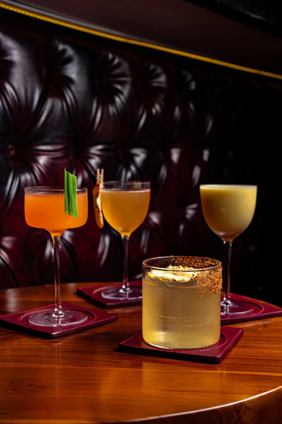 Four cocktails on a table in front of a leather banquette