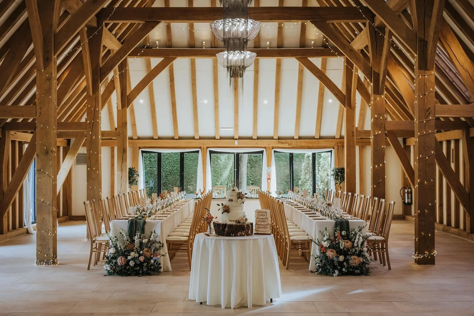 Long wedding reception tables set inside the oak-framed New Barn, at The Old Kent Barn, a wedding venue in Kent