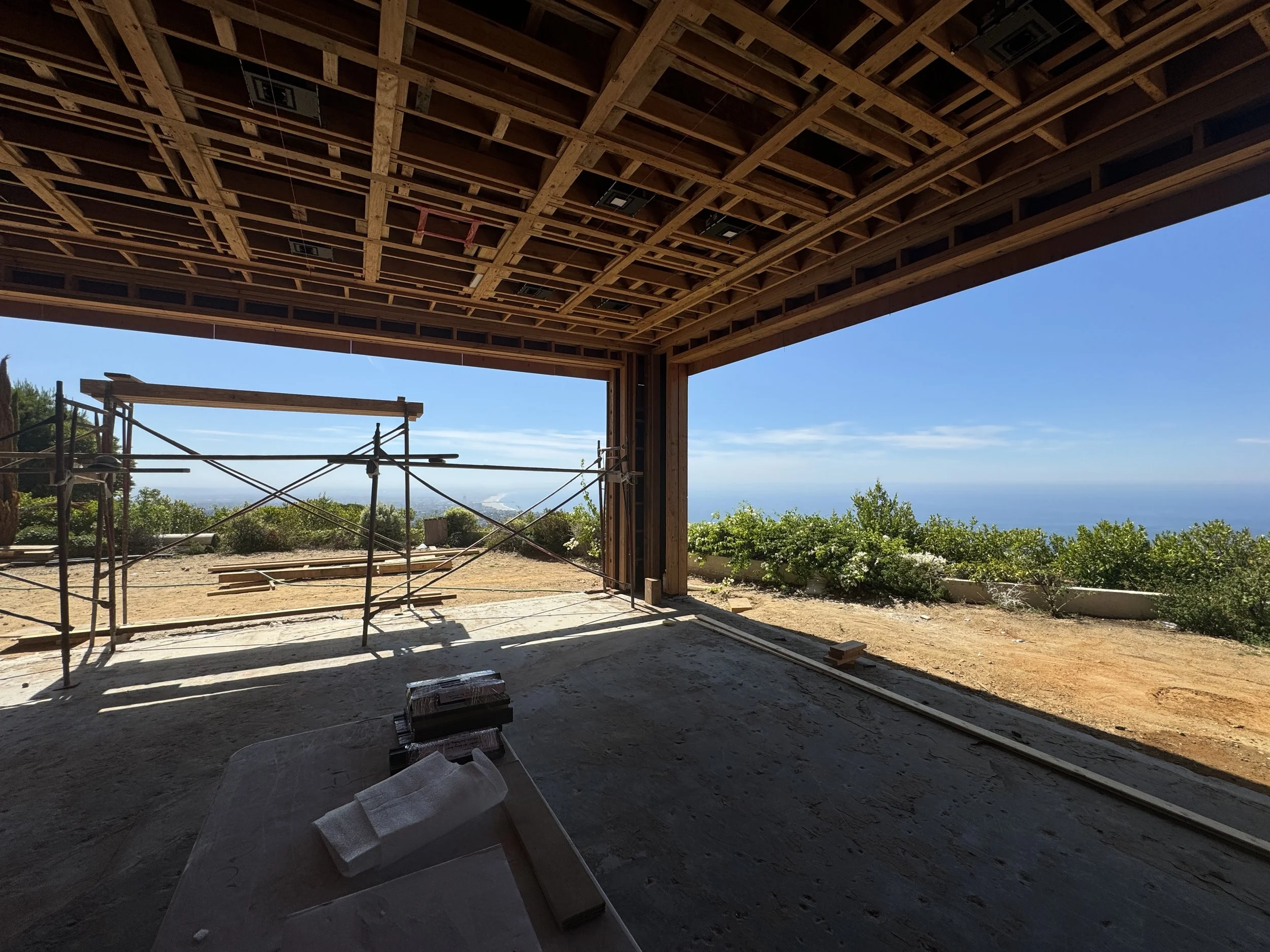 Construction framing of the living room, showing the coffered ceiling structure and large openings oriented toward the Pacific Ocean.