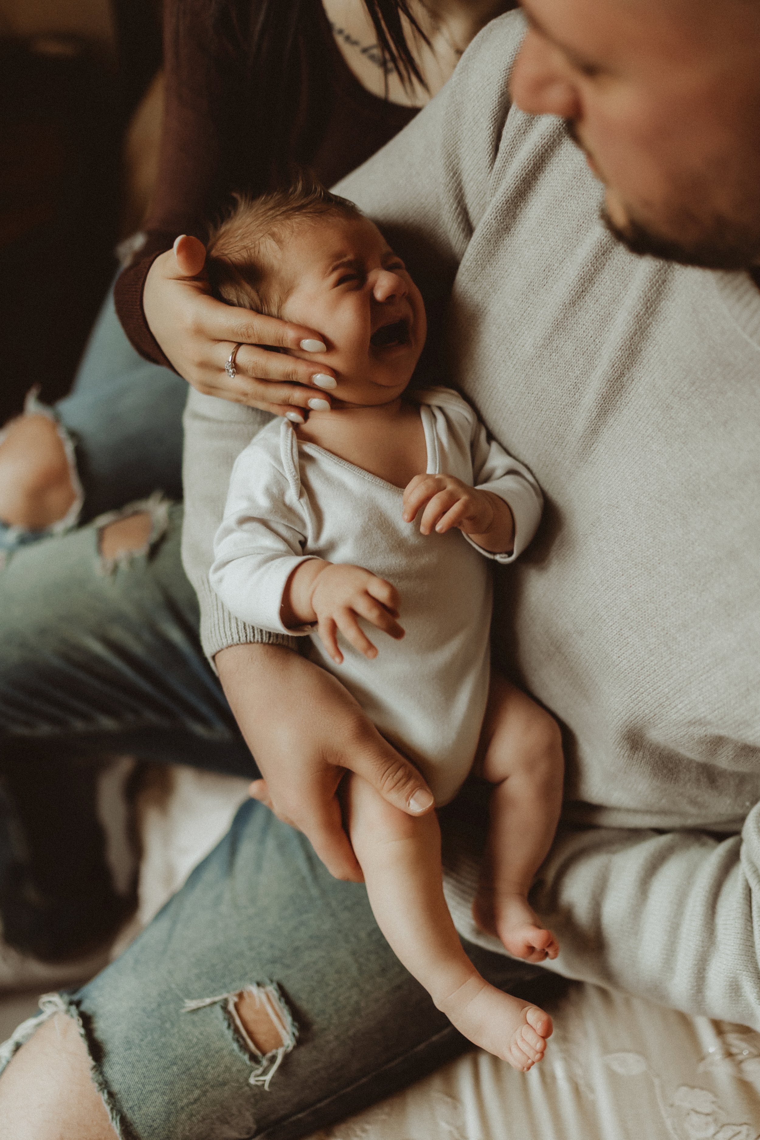 Un bambino sta piangendo tra le braccia di un uomo, mentre una donna lo conforta stringendo la testa del bambino.