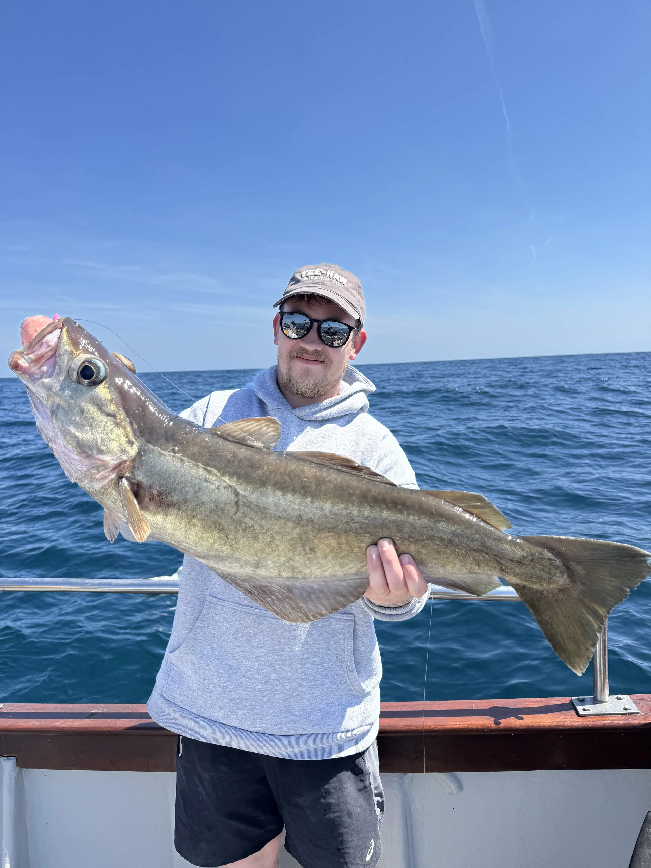 Man holding a large fish on a boat at sea under a blue sky
