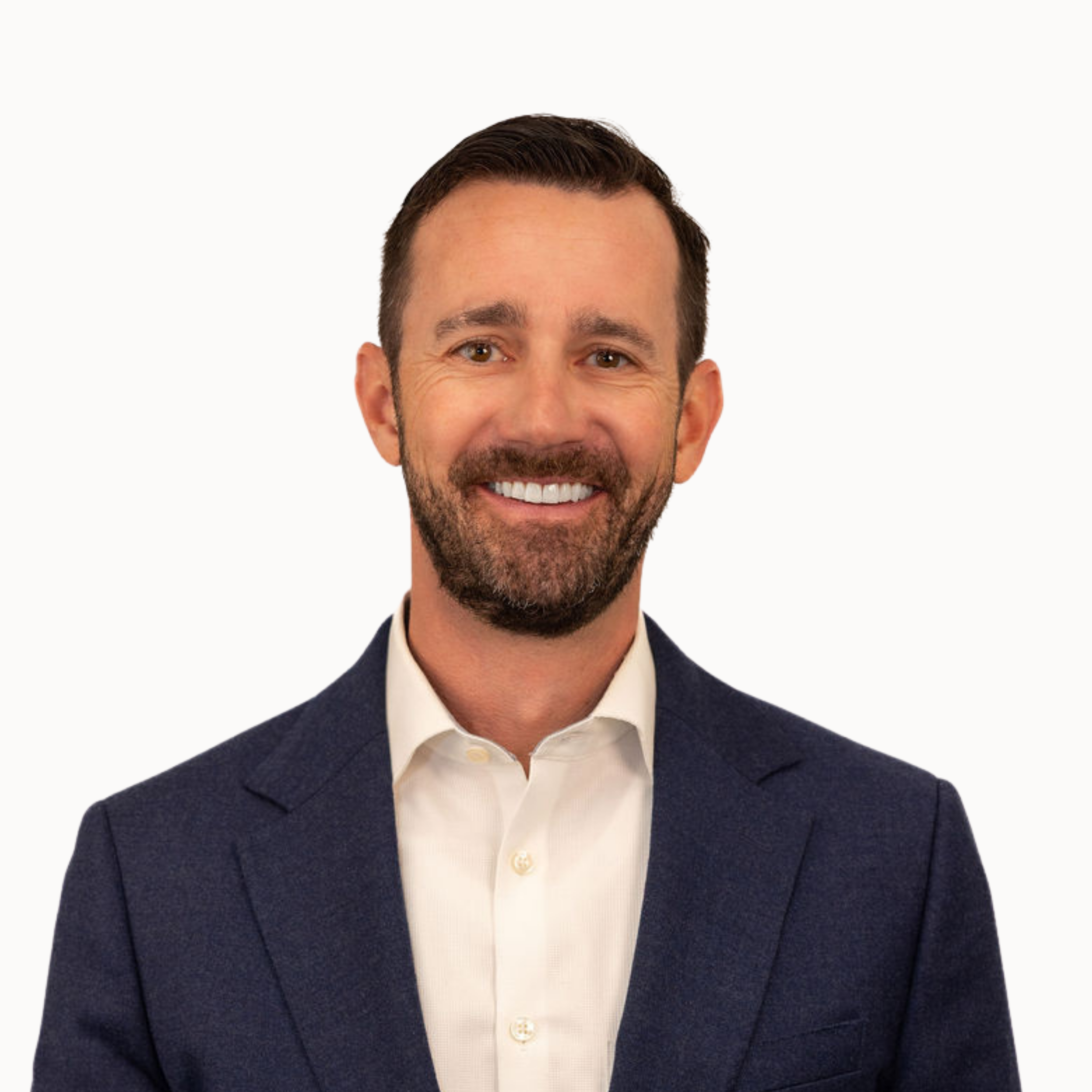 Headshot of a smiling man with dark hair and a beard, wearing a dark blazer and white shirt against a gray background.