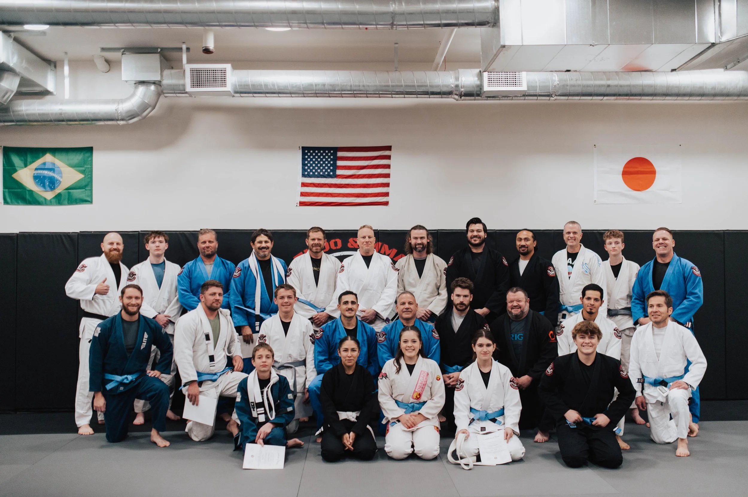 Martial arts students and instructor practicing techniques in a gym with exposed ceiling beams.