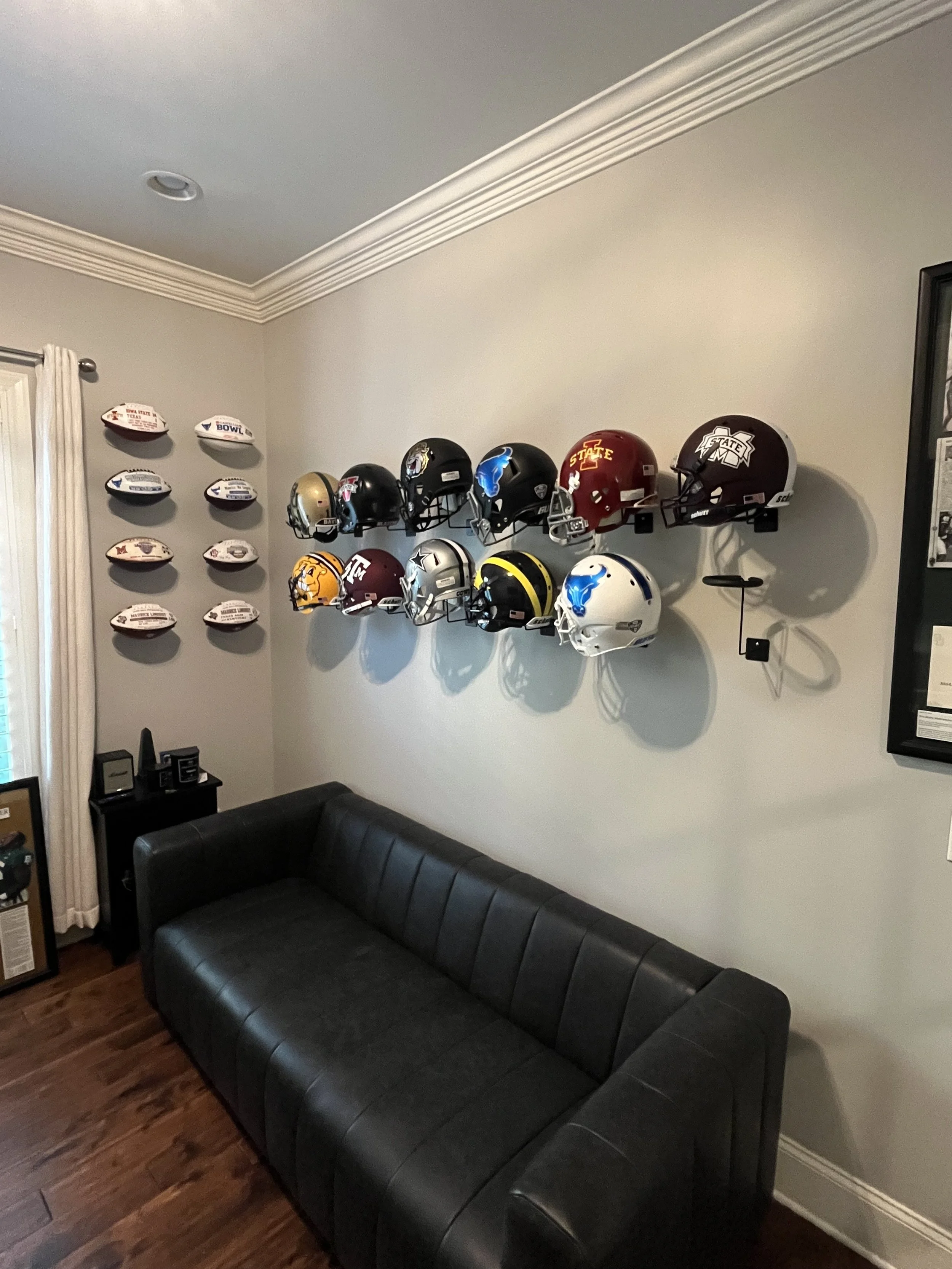 Wall with football helmets and mini footballs displayed, next to black leather couch in a room.