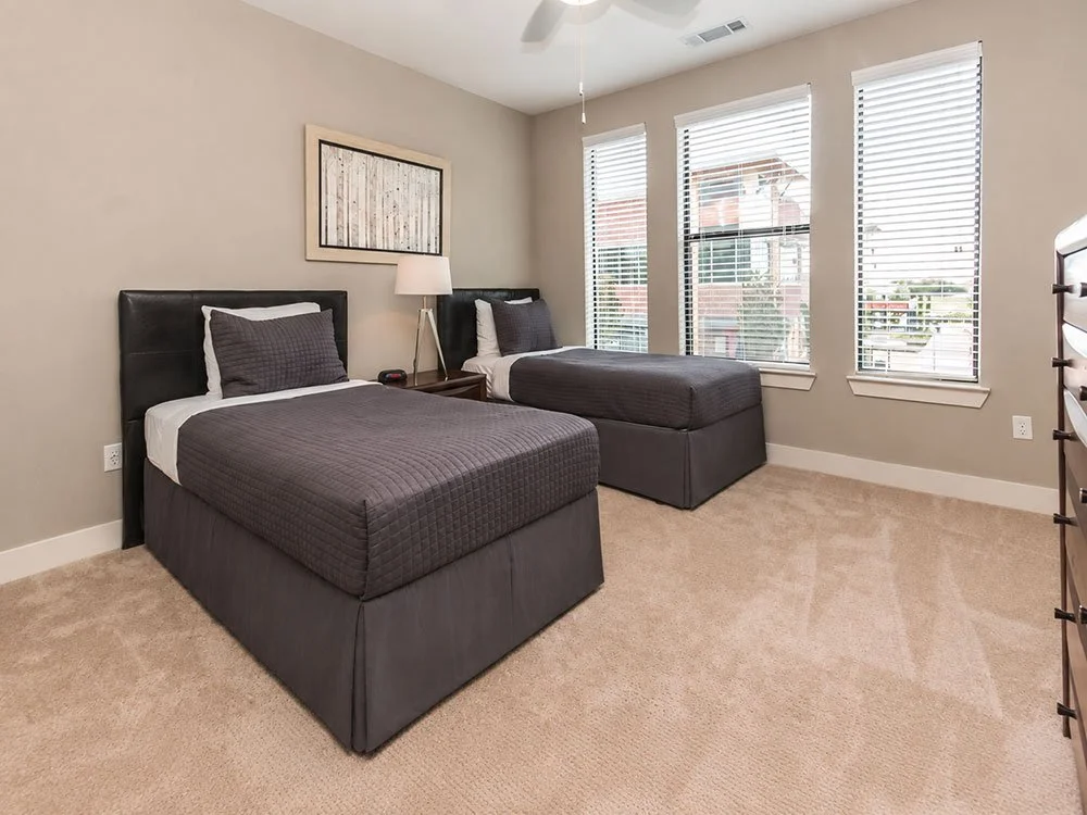 A bedroom furnished with rental furniture from Furniture Options, with two twin beds and matching dark gray bedding, positioned side by side. Perfect for shared temporary living.