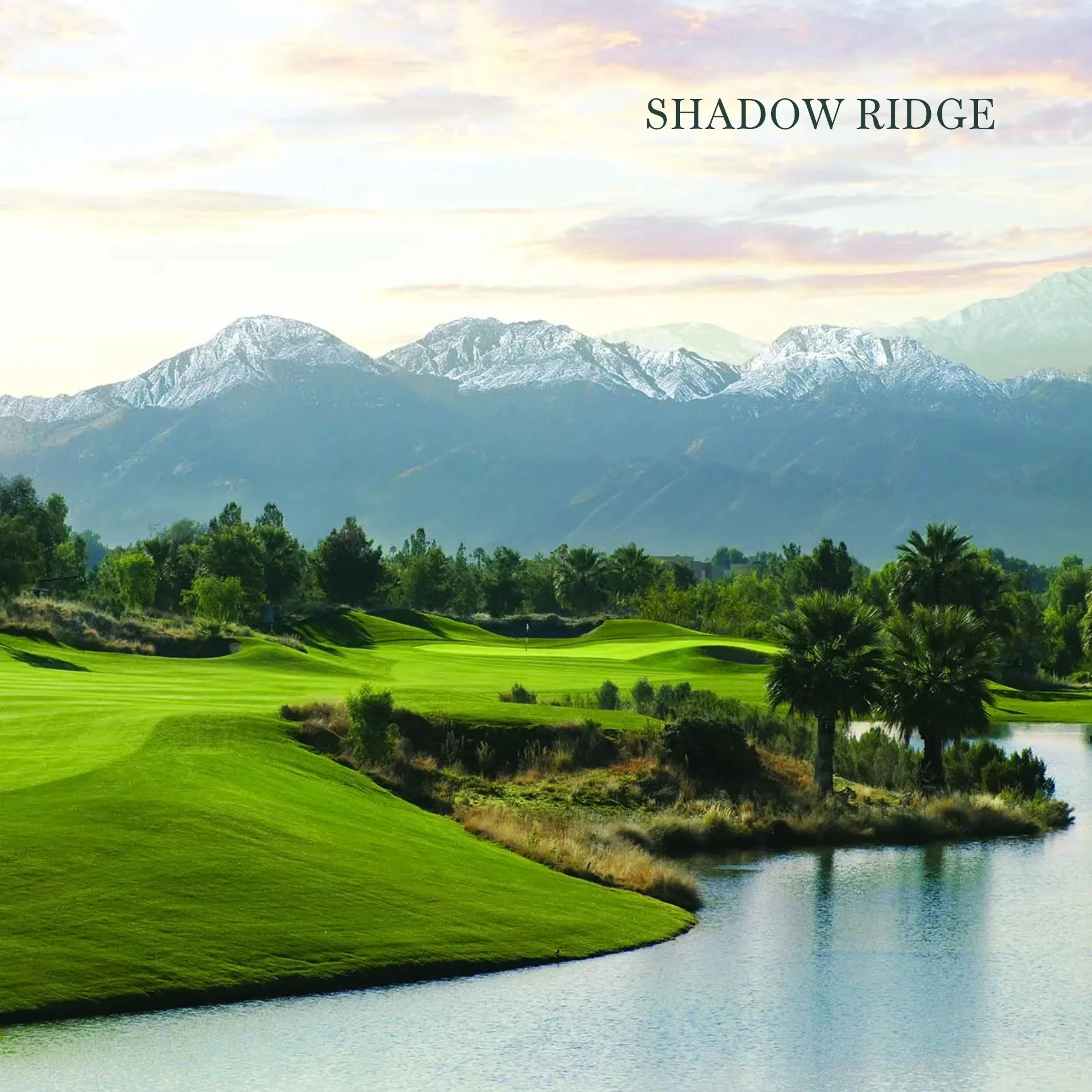 Scenic view of a golf course with green fairways, water hazards, and trees, with snow-capped mountains in the background and a partly cloudy sky. The text 'Shadow Ridge' appears in the top right corner.