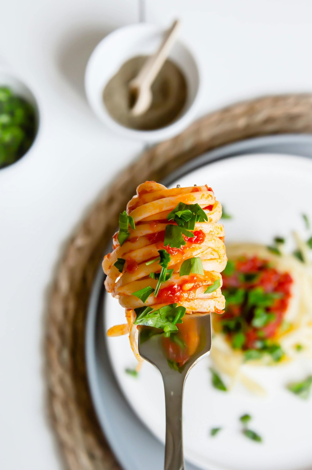 Spaghetti with marinara and herbs wrapped around a fork with a plate in the background.jpg