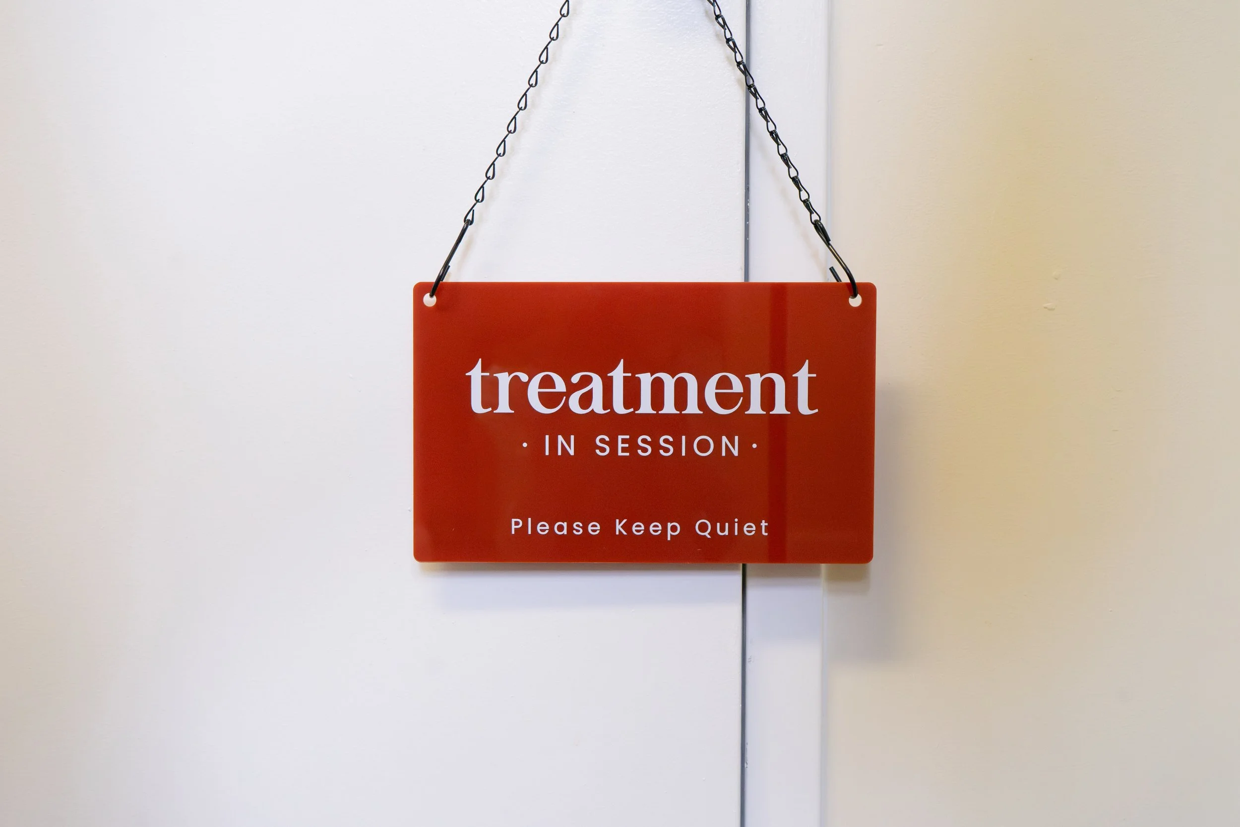 Red sign hanging on a door that says 'treatment in session. Please keep quiet.'