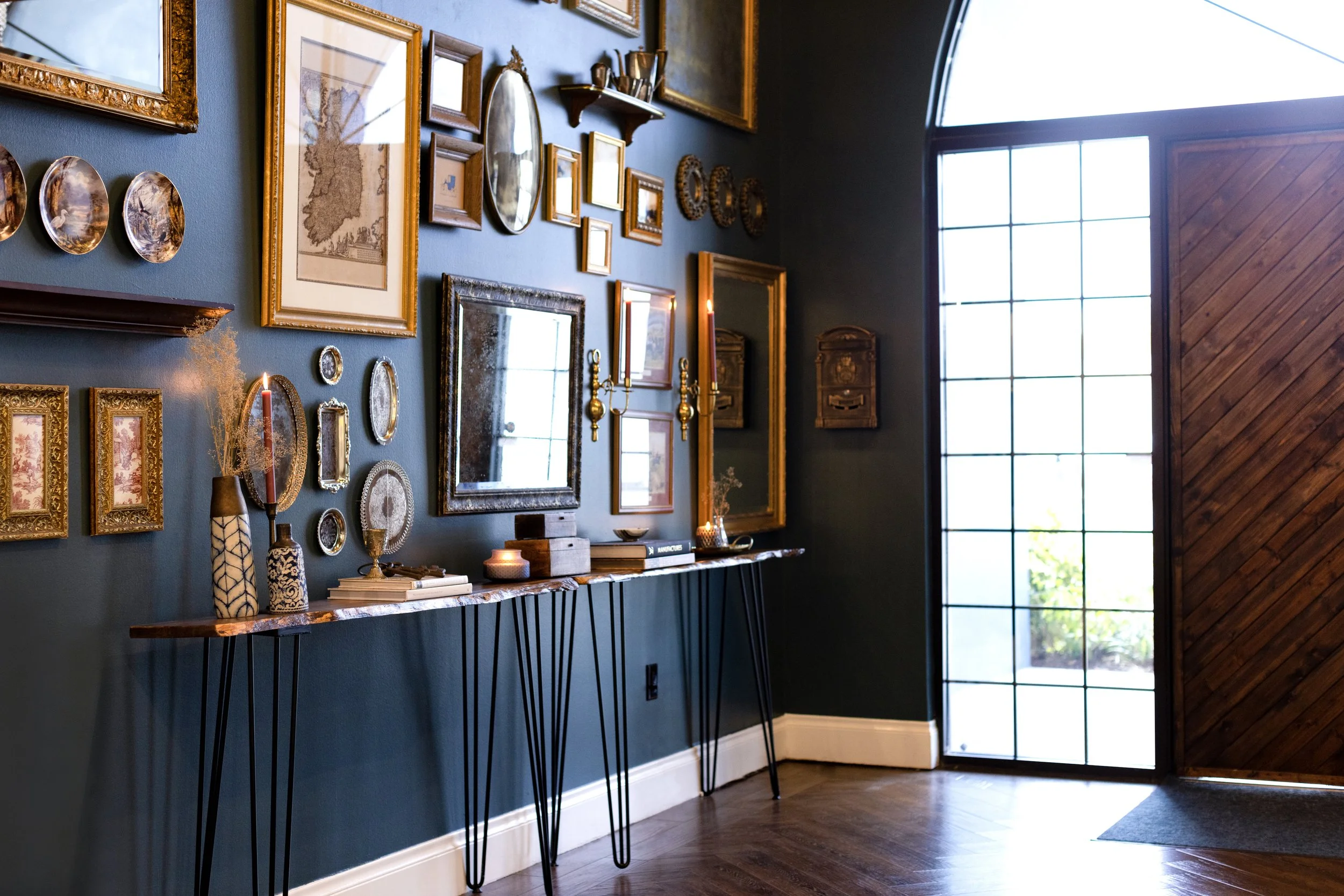 A dramatic entryway featuring antique statement art, moody and natural lighting, dark blue paint, a curated console table, gold leafing on the ceiling