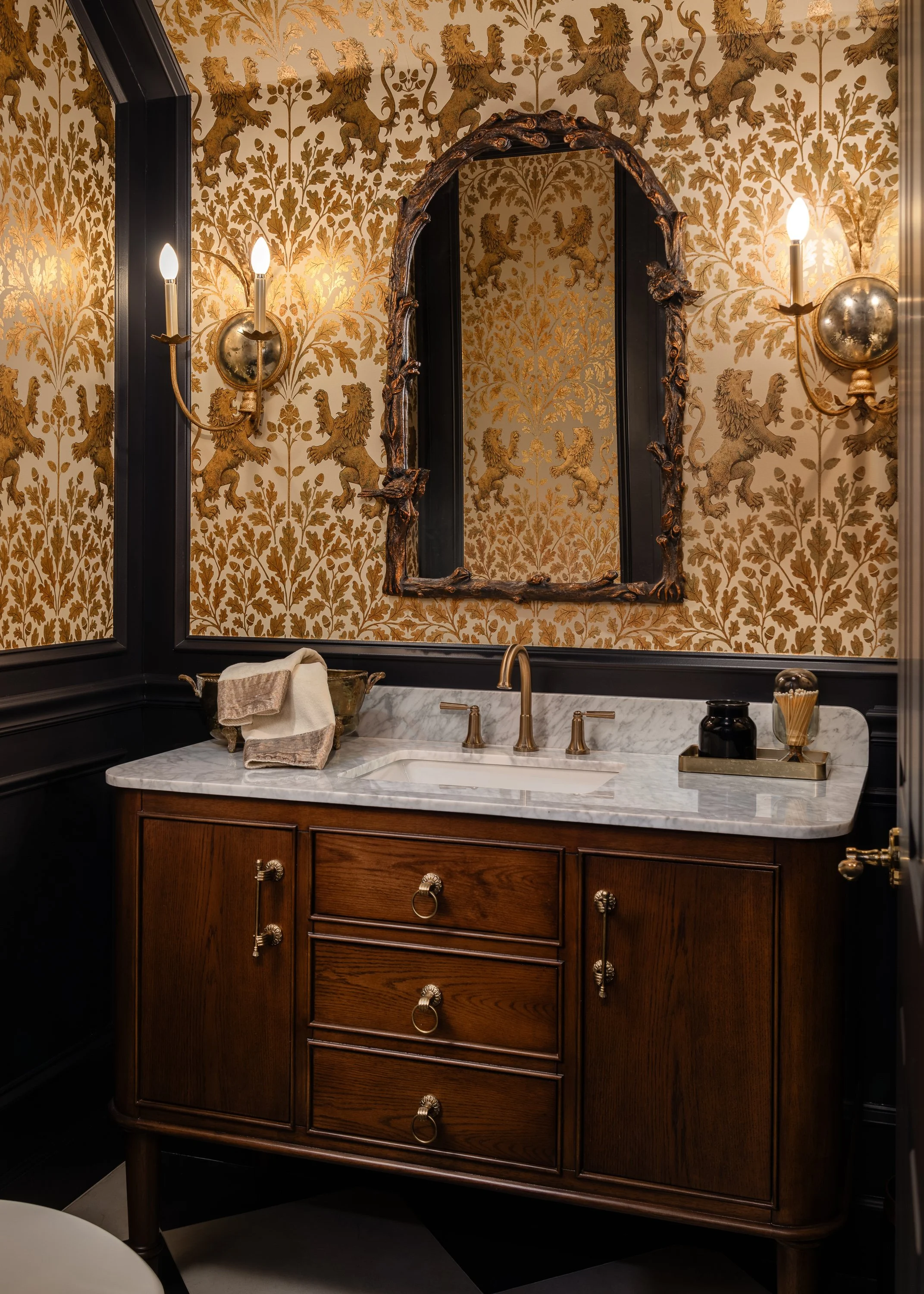 A powder room with gold lion and oak leaf wallpaper, a dark wood vanity with a marble top, and an ornate mirror above the sink. Carrollwood Area, Tampa, FL