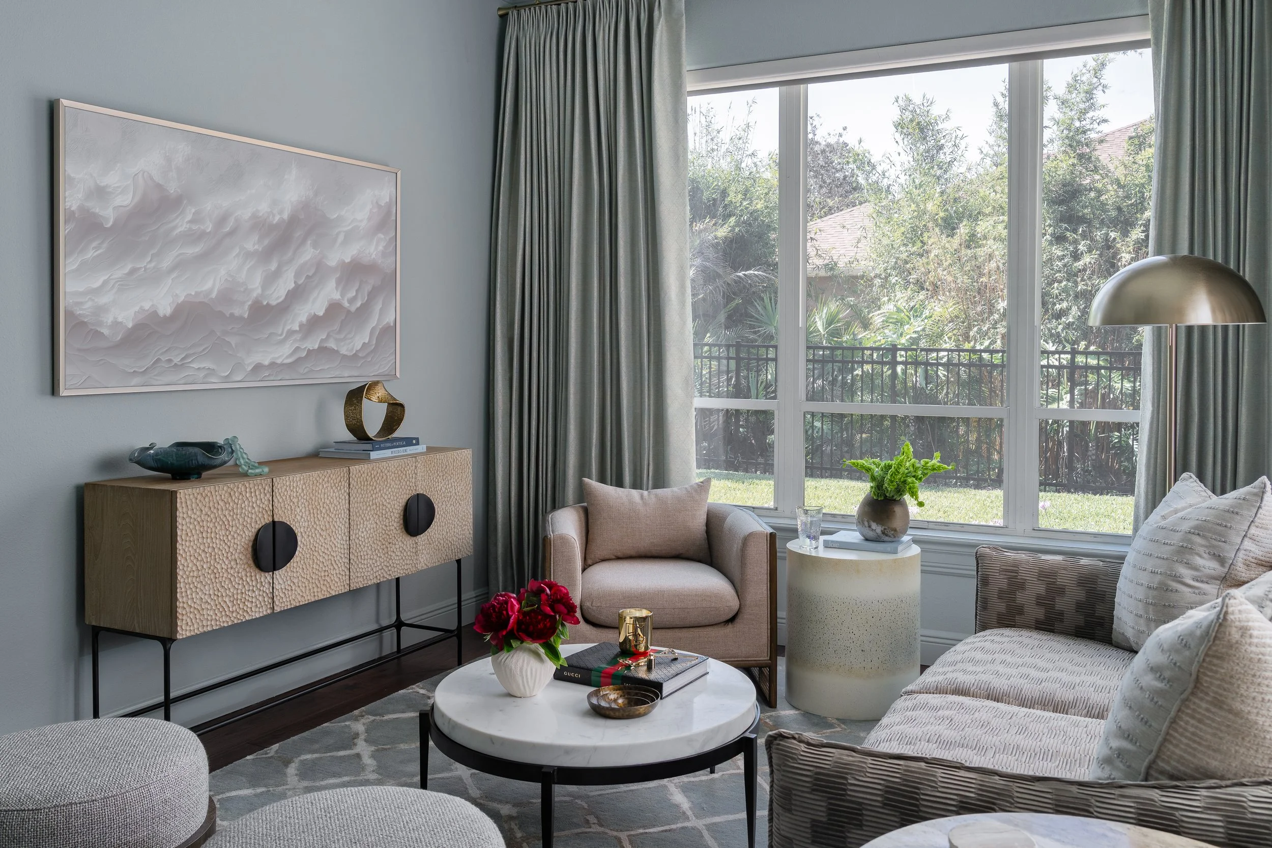 A stylish contemporary modern sunroom design with a textured console table, a large abstract artwork, plush seating, and a round coffee table adorned with flowers and books.