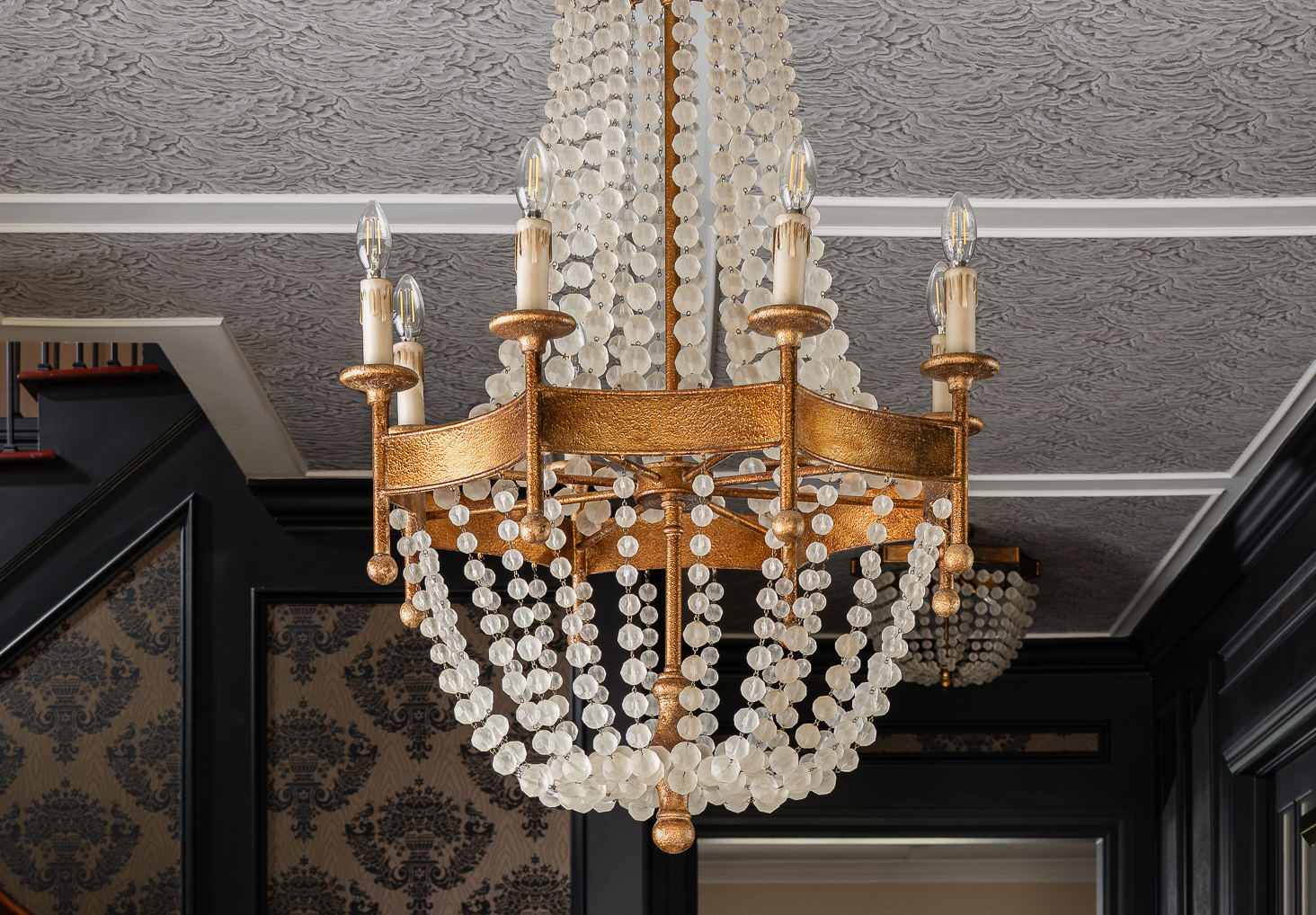 A gold chandelier with crystal beads and candle-shaped lights hangs from a textured gray ceiling.