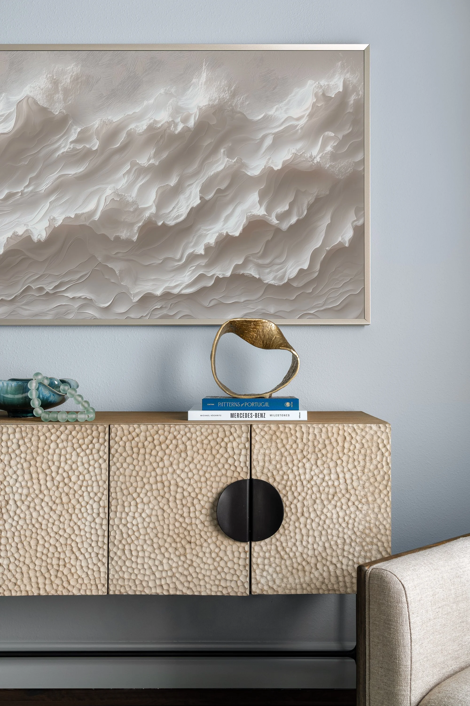 contemporary modern sunroom design A textured wooden cabinet with a circular handle sits below a framed abstract artwork of layered white and beige forms.