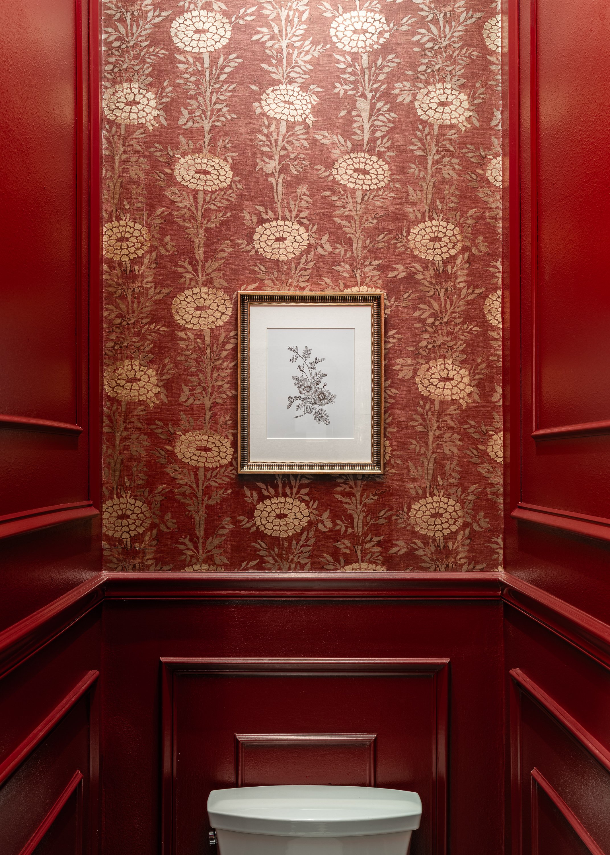 Commercial restroom design. A framed botanical print hangs on a wall with red floral wallpaper and dark red wainscoting. A white toilet is visible at the bottom.