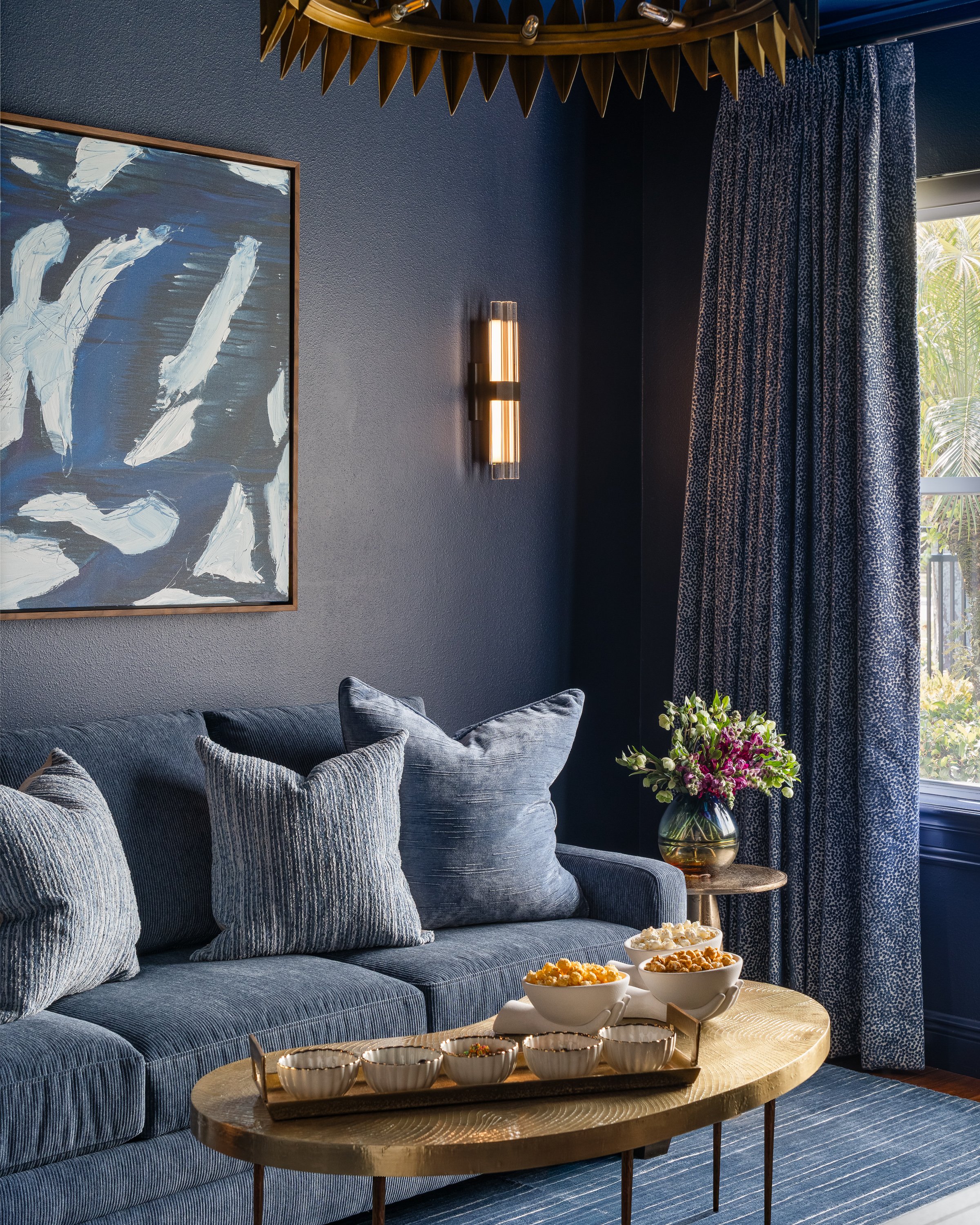 Contemporary modern sunroom design A cozy living room with a blue sofa, abstract blue and white art, patterned curtains, and a coffee table with bowls of popcorn.