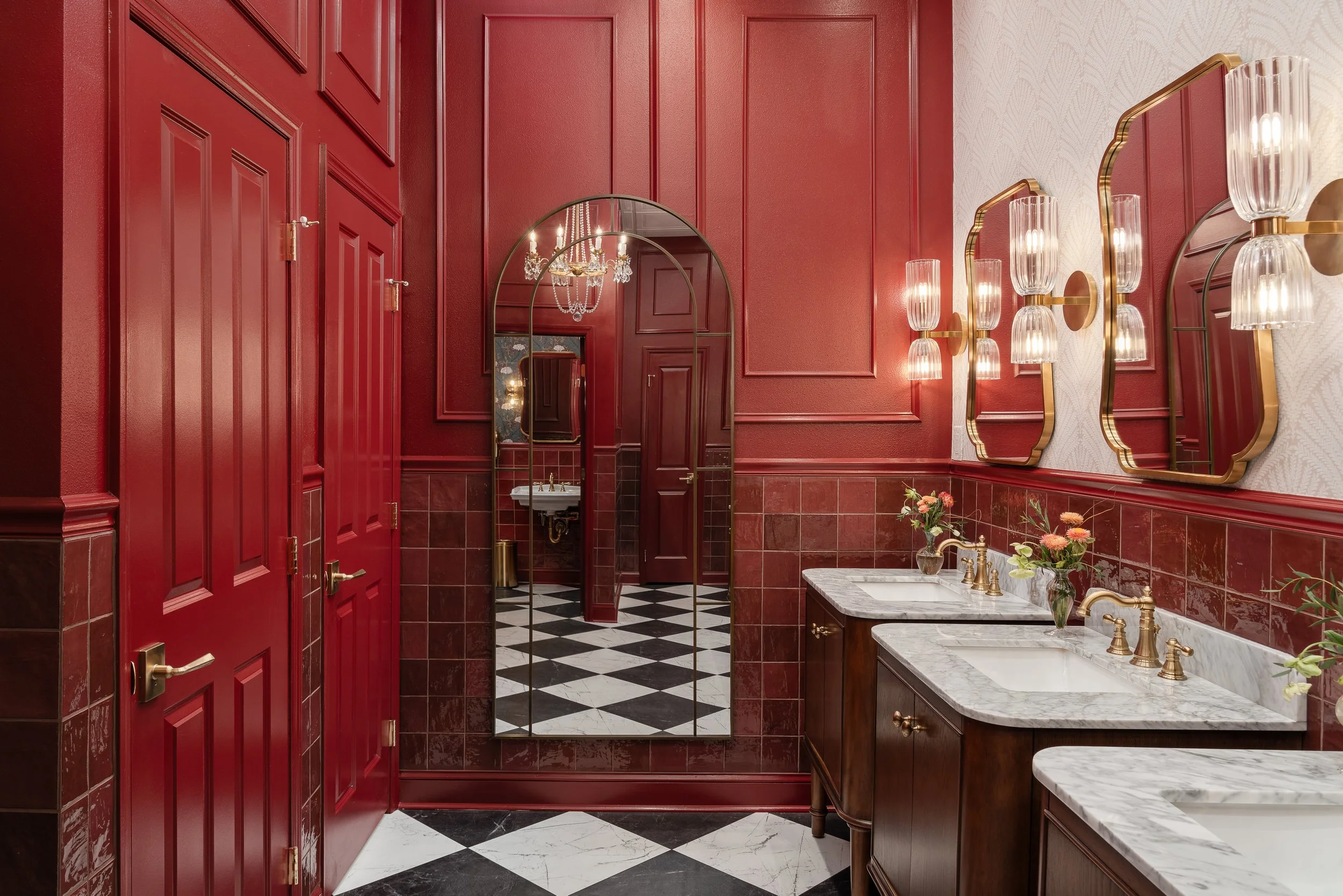 A luxurious red bathroom with a black and white checkered floor, multiple sinks with marble countertops, and ornate gold fixtures. Mirrors with gold frames reflect the room's opulent design.