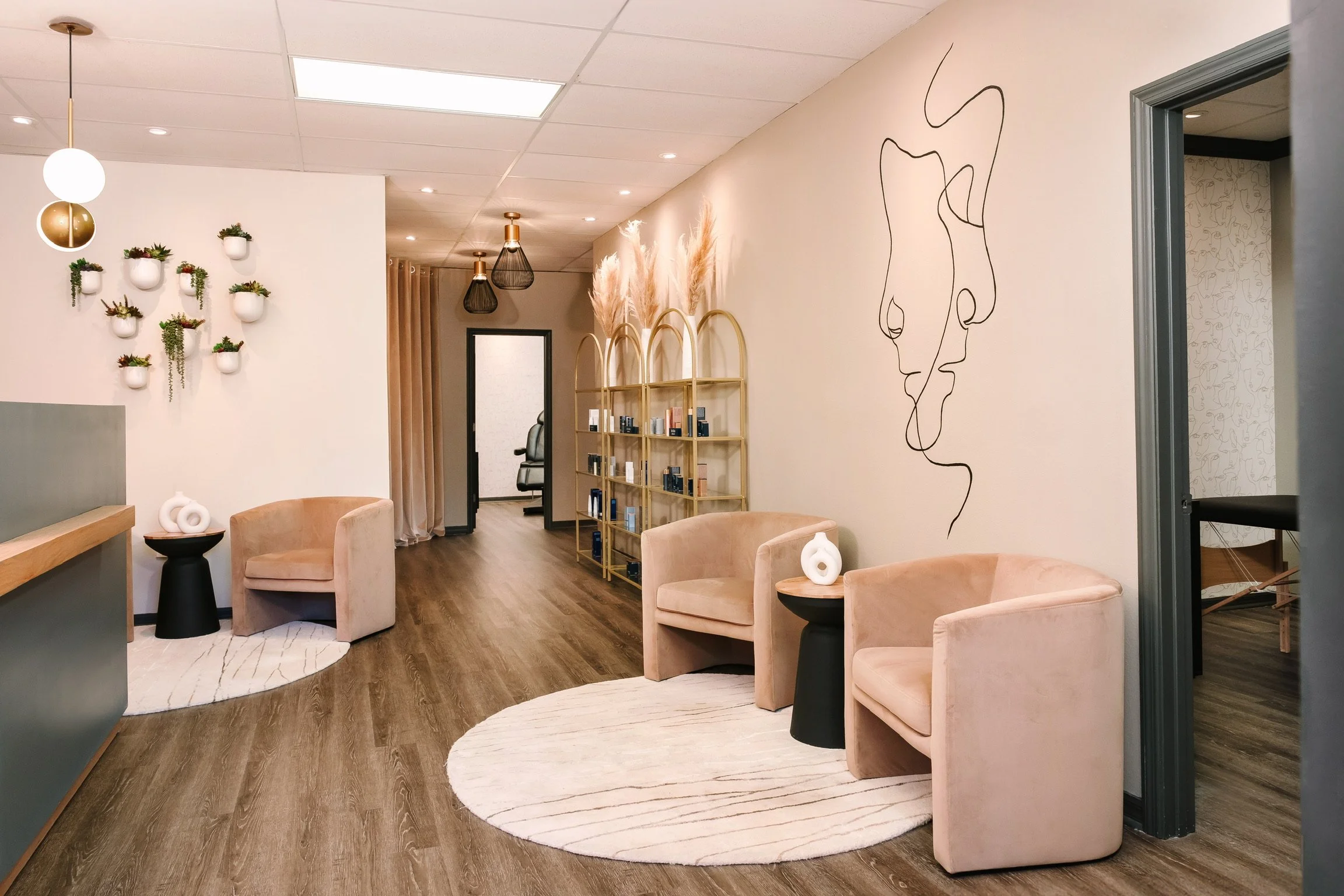 A spacious and modern spa lobby and waiting area with warm wood floors, comfortable seating areas, and a reception desk round rugs defining spaces, living plants on the wall and a custom mural.