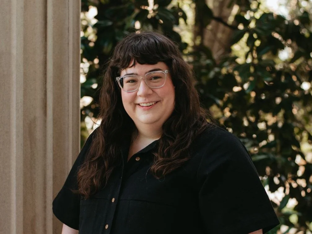 A woman with brown hair and glasses is smiling next to a limestone column.