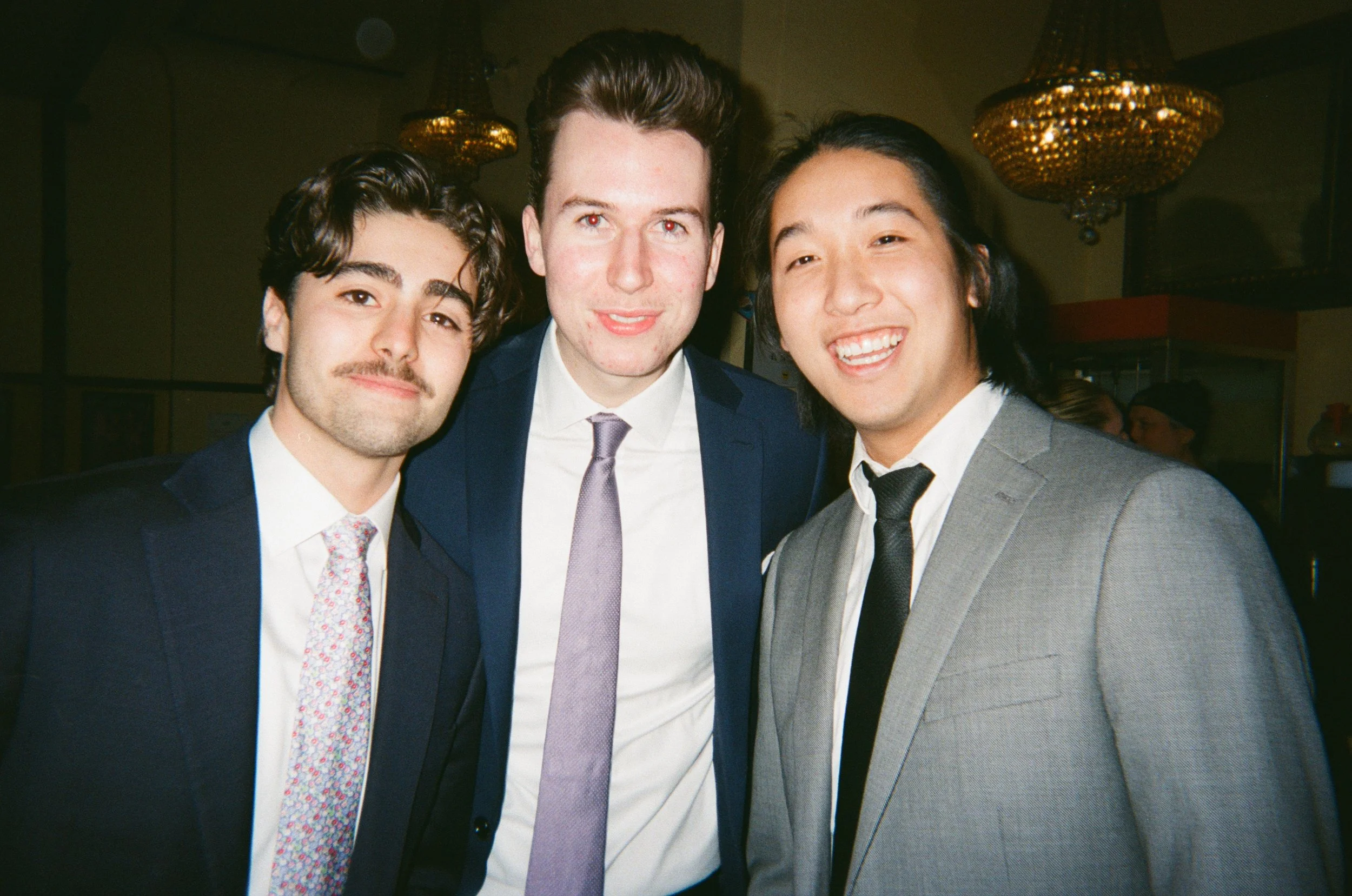Three young men in suits smiling at a social event.