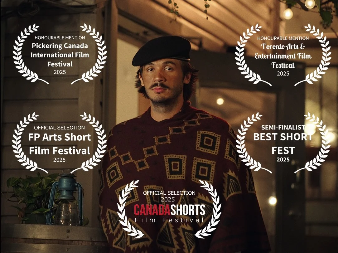 A young man wearing a patterned sweater and a black beret standing indoors with awards from various film festivals displayed around him.